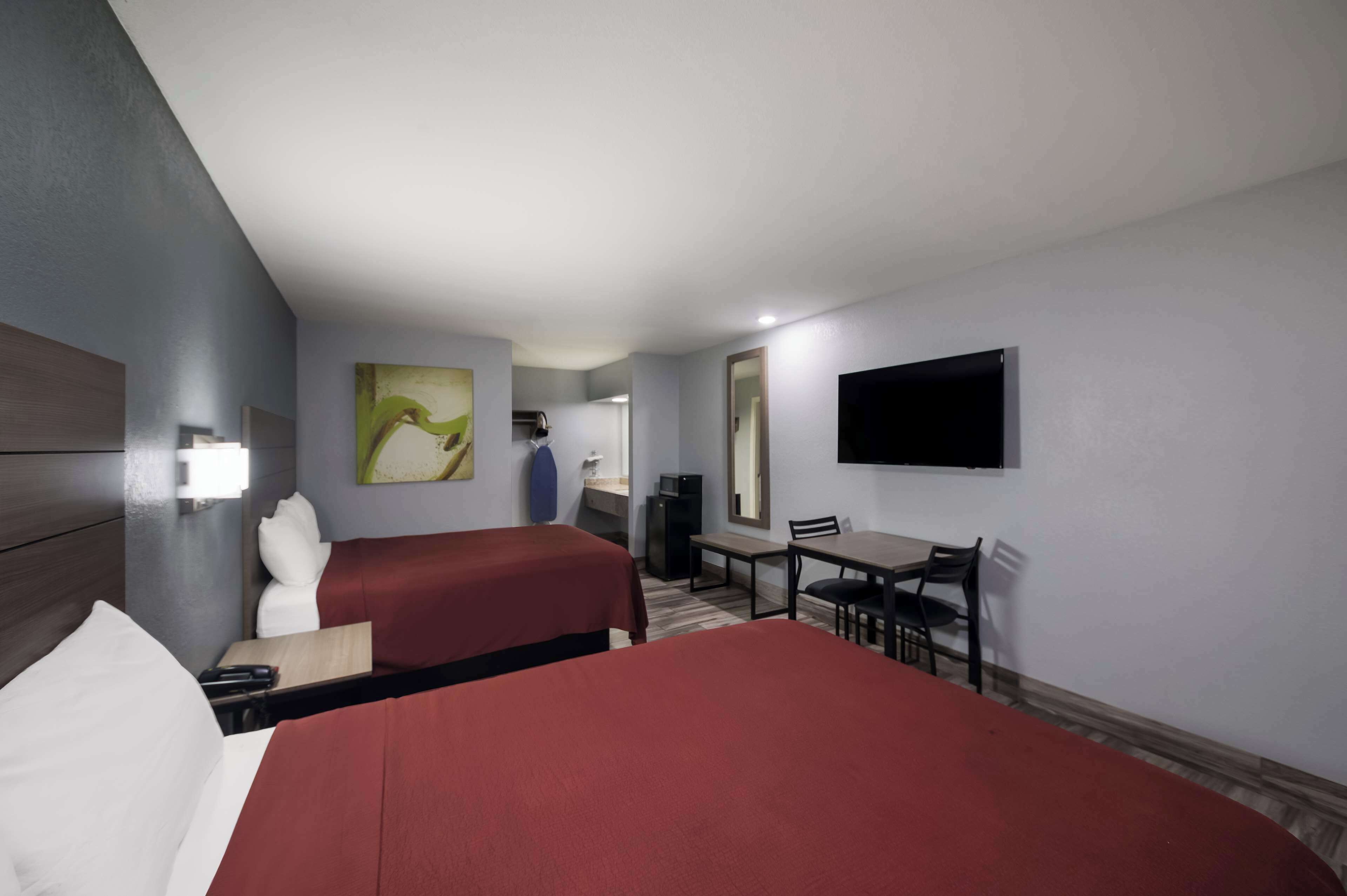 A hotel room with two beds, a desk, a chair, a television, and a painting on the wall.