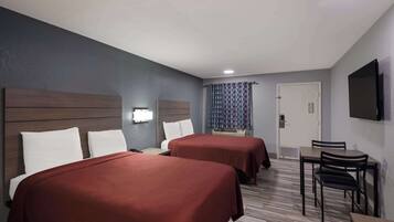 A hotel room with two beds, a desk, a chair, a TV, and a door.