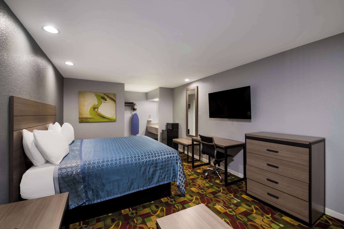 A hotel room with a bed, desk, chair, dresser, and a television on the wall.