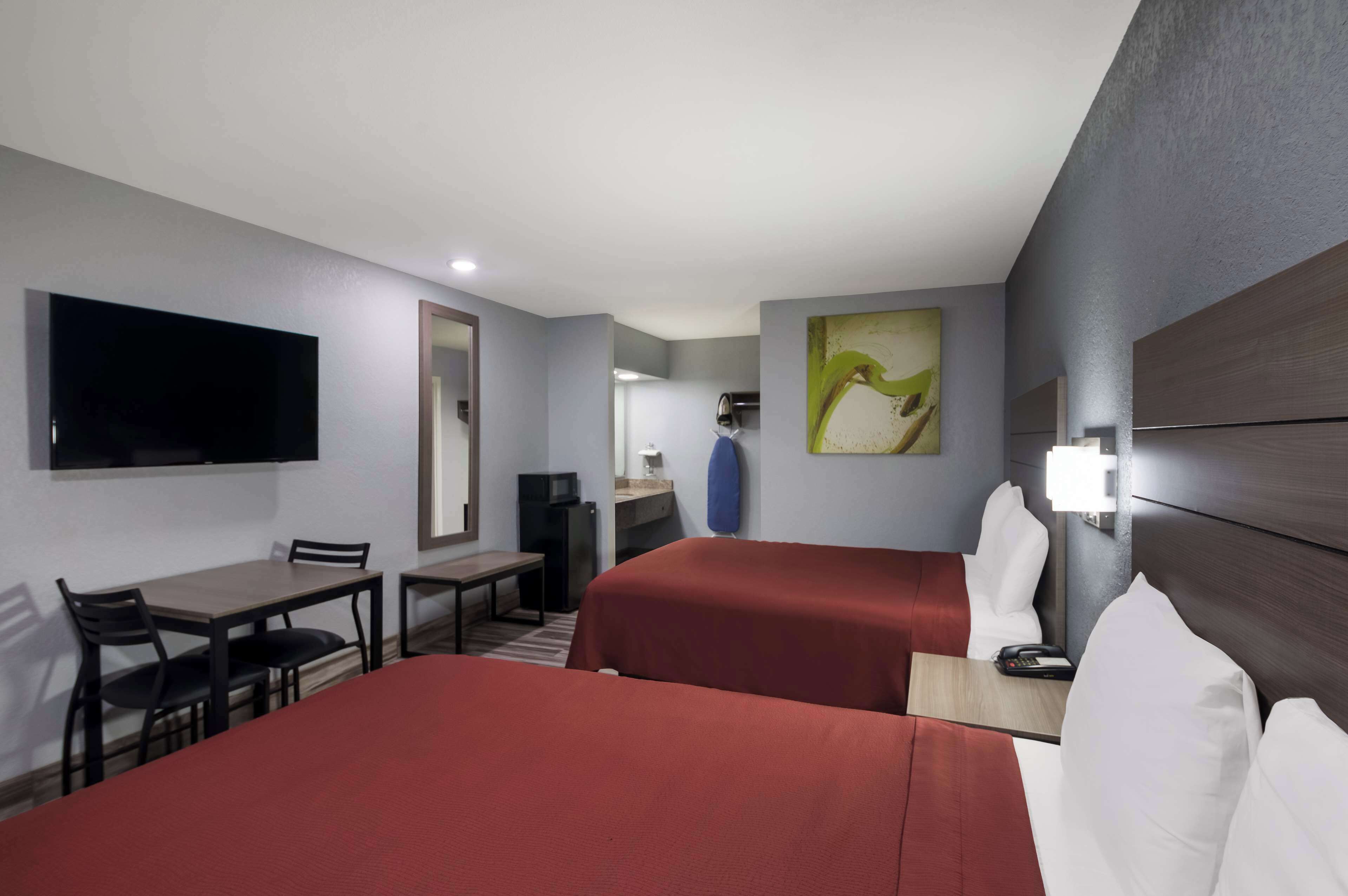 A hotel room with two beds, a desk, a chair, a television, and a painting on the wall.