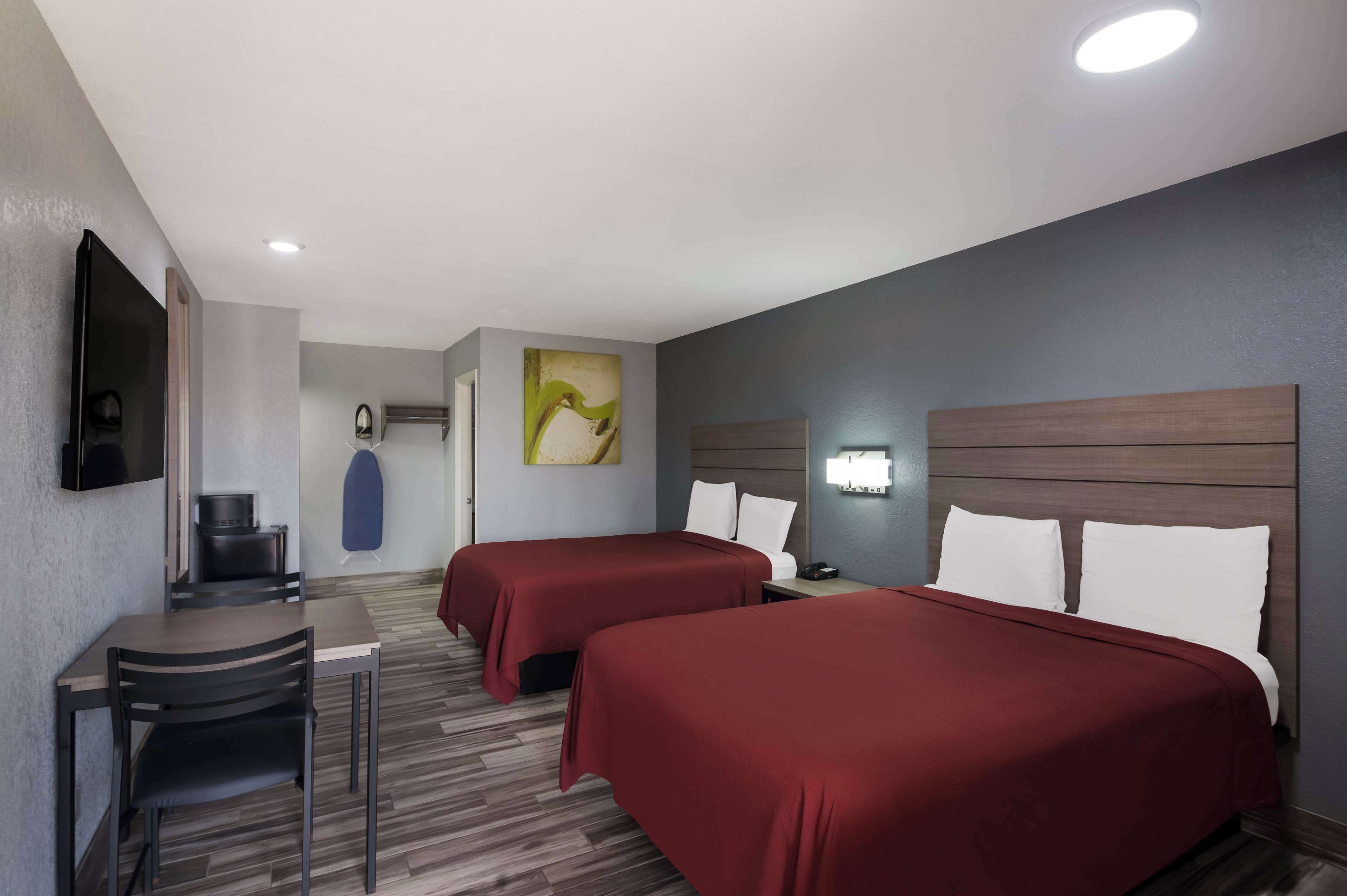 Habitación de hotel con dos camas, un escritorio, una silla, un televisor y un cuadro en la pared.
