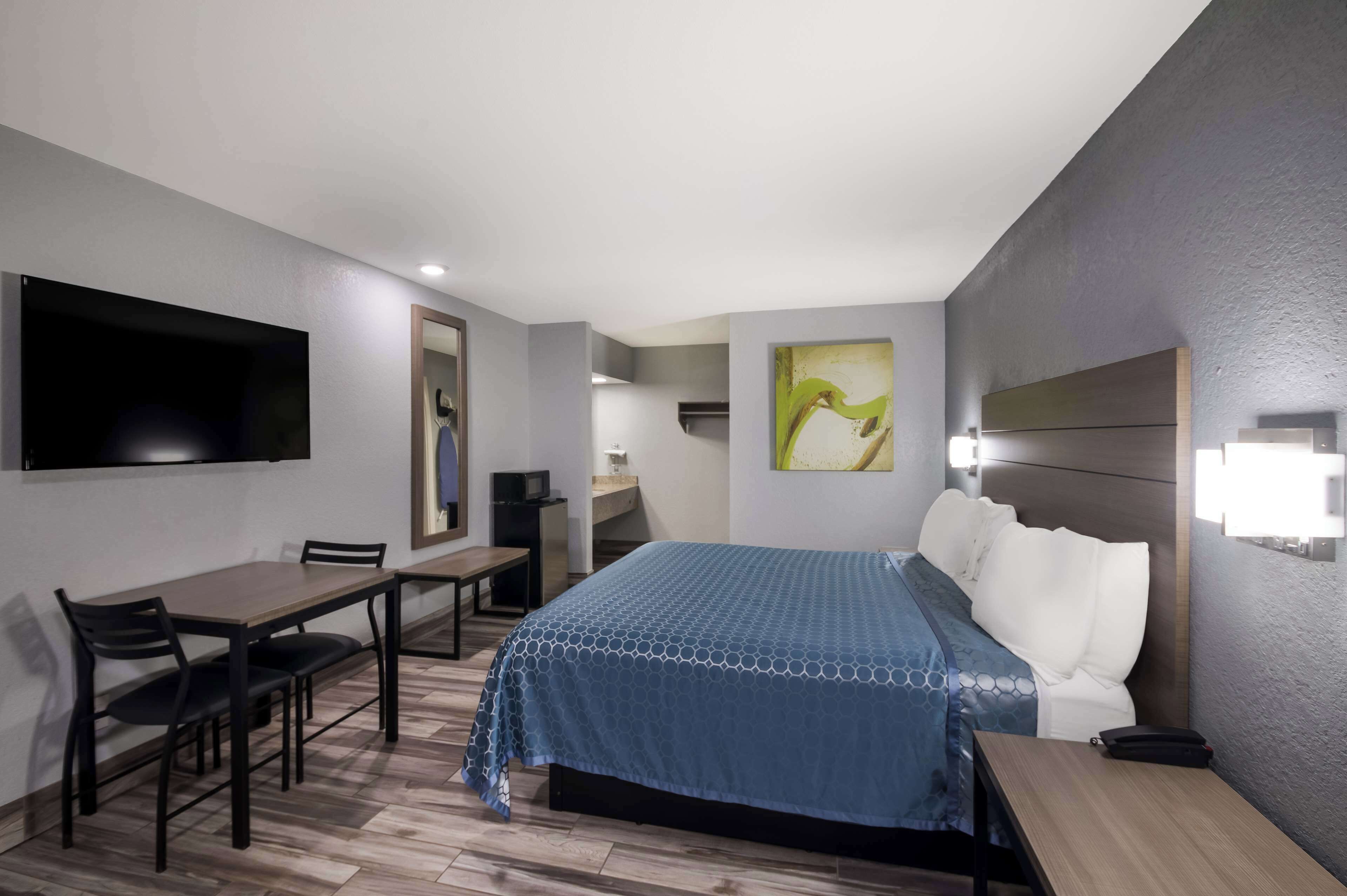 Habitación de hotel con cama, escritorio, silla, televisor montado en la pared y obras de arte en las paredes.