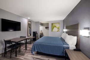 Habitación de hotel con cama, escritorio, silla, televisor montado en la pared y obras de arte en las paredes.