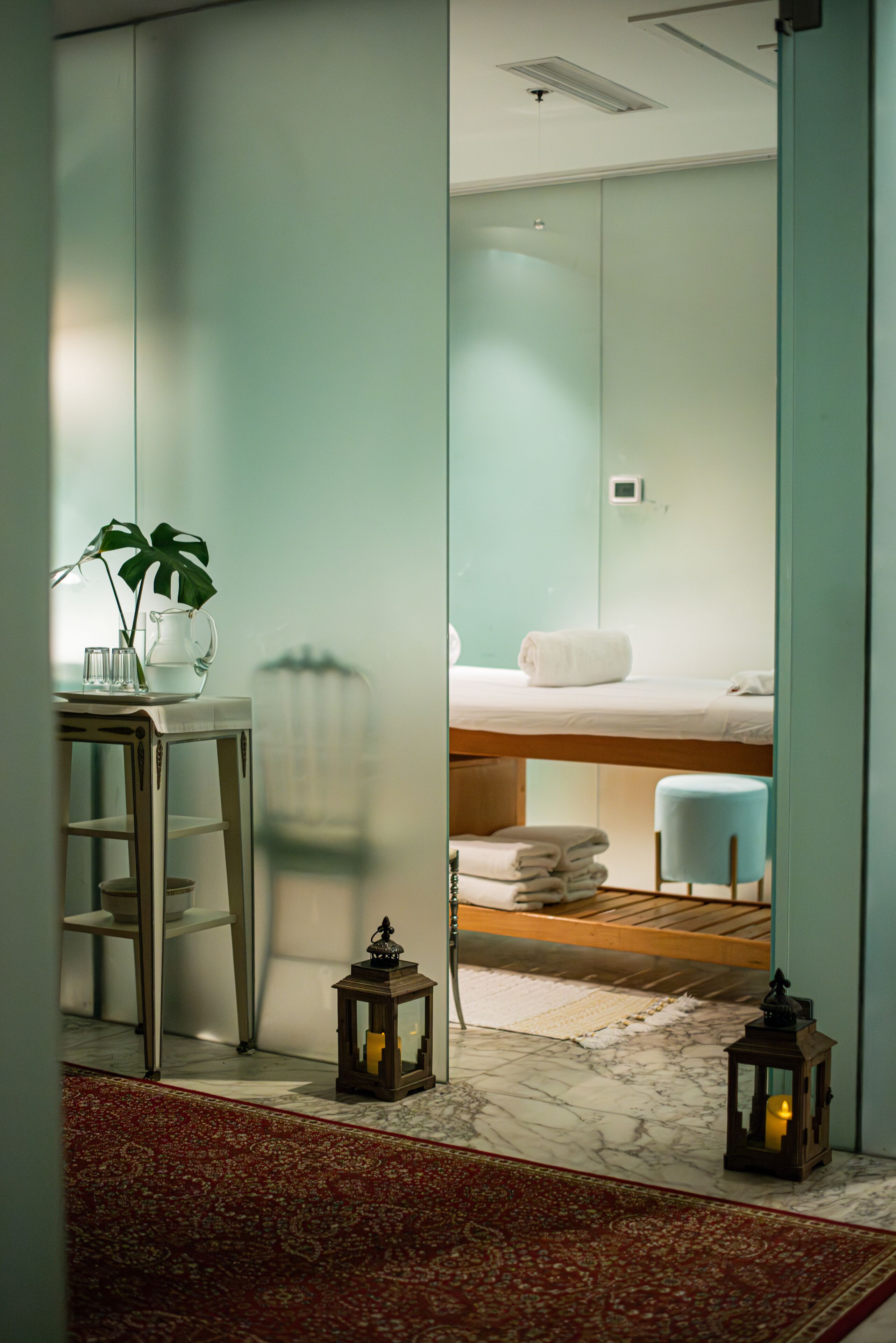 Una habitación de hotel moderna con una cama, una mesita con una planta, un espejo y una alfombra roja.
