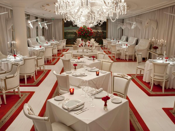 Un comedor formal con mesas y sillas blancas, y una lámpara de araña.