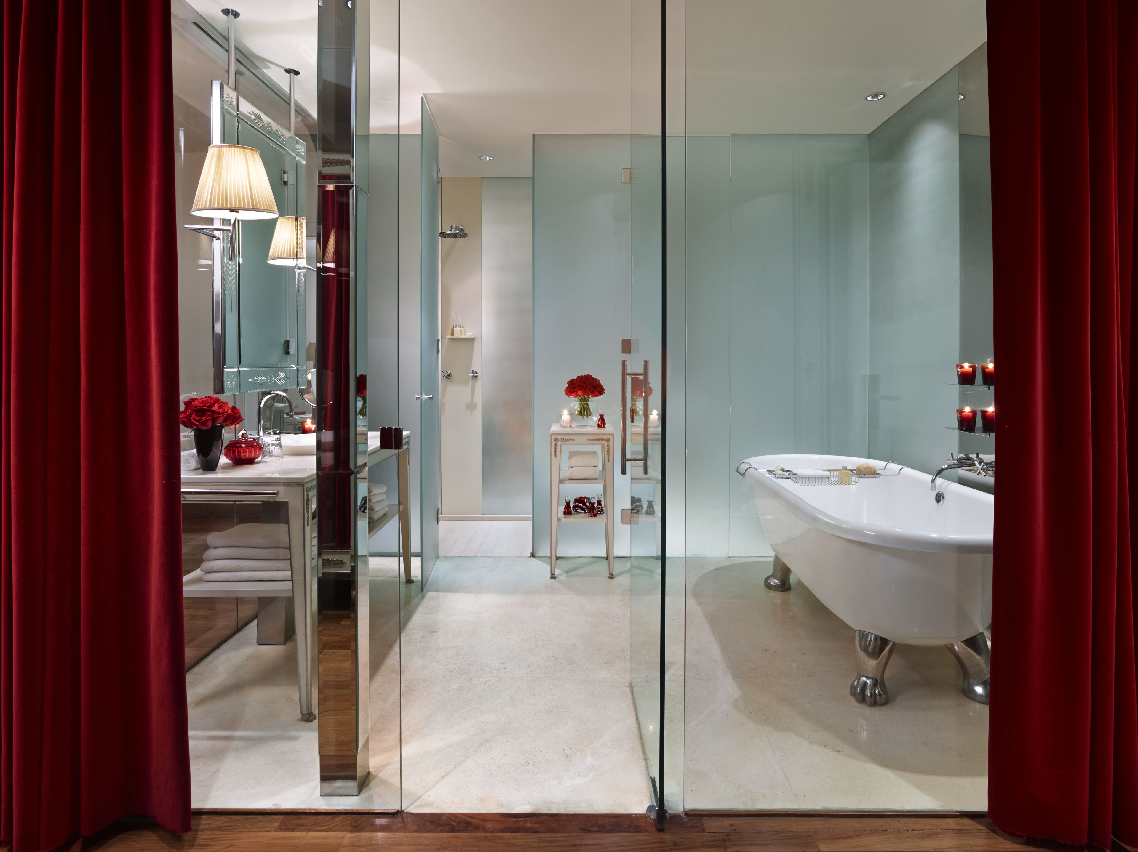 Un baño moderno con mampara de vidrio, una bañera blanca y un tocador con espejo y rosas rojas.