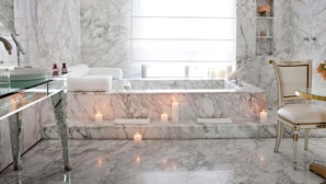 A marble bathroom with a bathtub, candles, a glass vanity, and a chair. - Faena Hotel Buenos Aires (Buenos Aires)