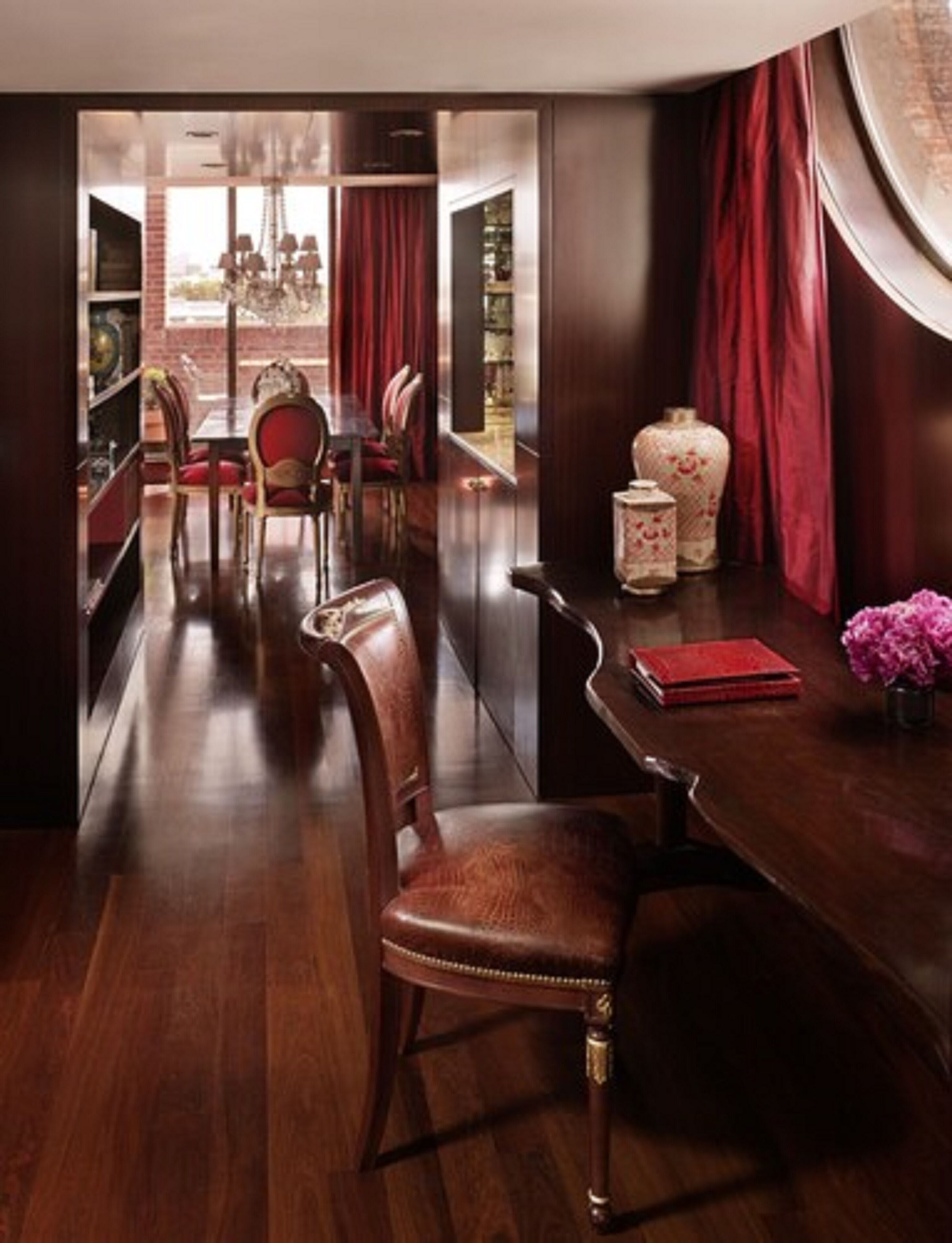 Comedor con muebles de madera, cortinas rojas y un florero con flores.