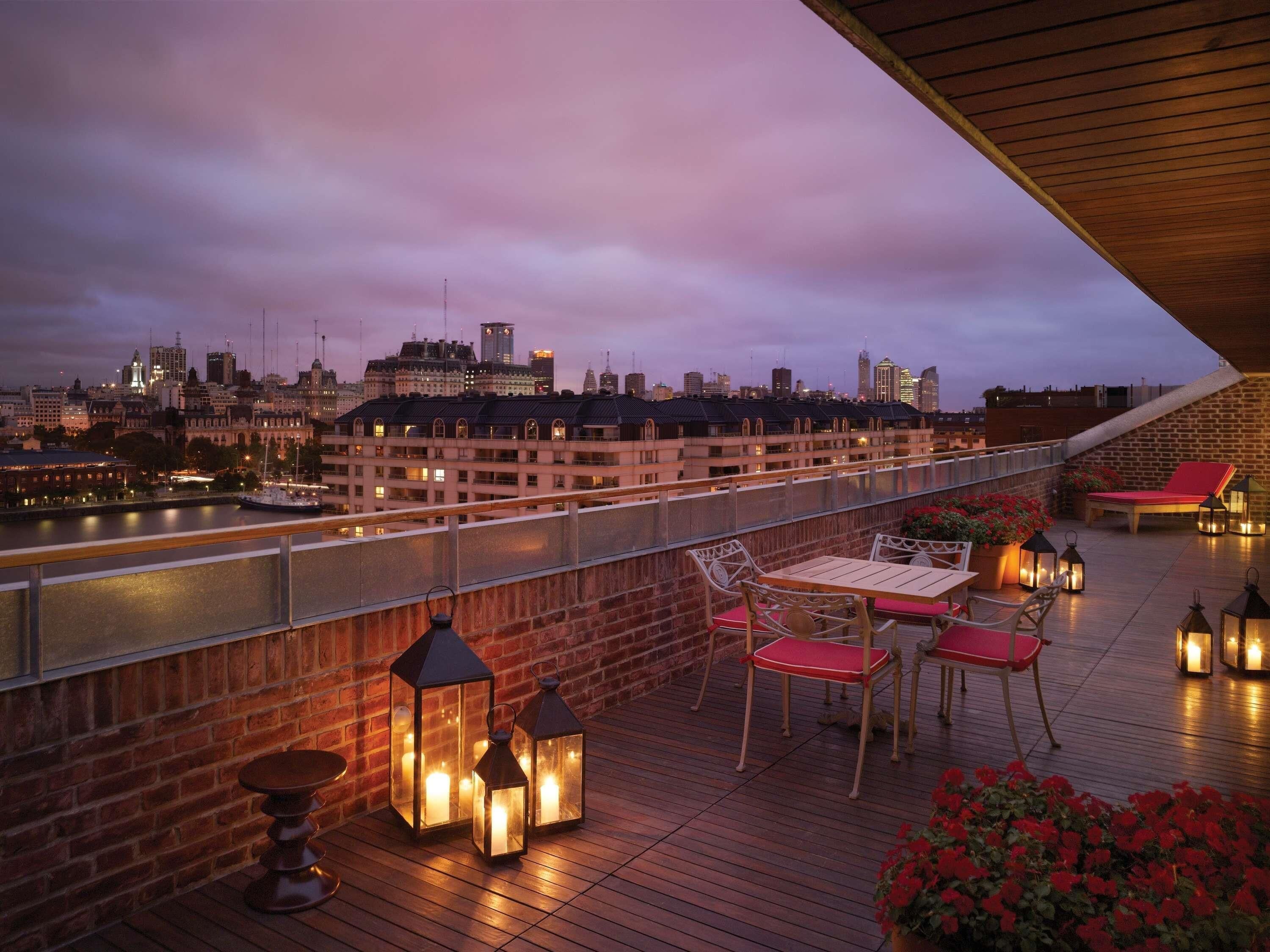 Terraza en la azotea con vistas al horizonte urbano, mobiliario exterior y faroles.