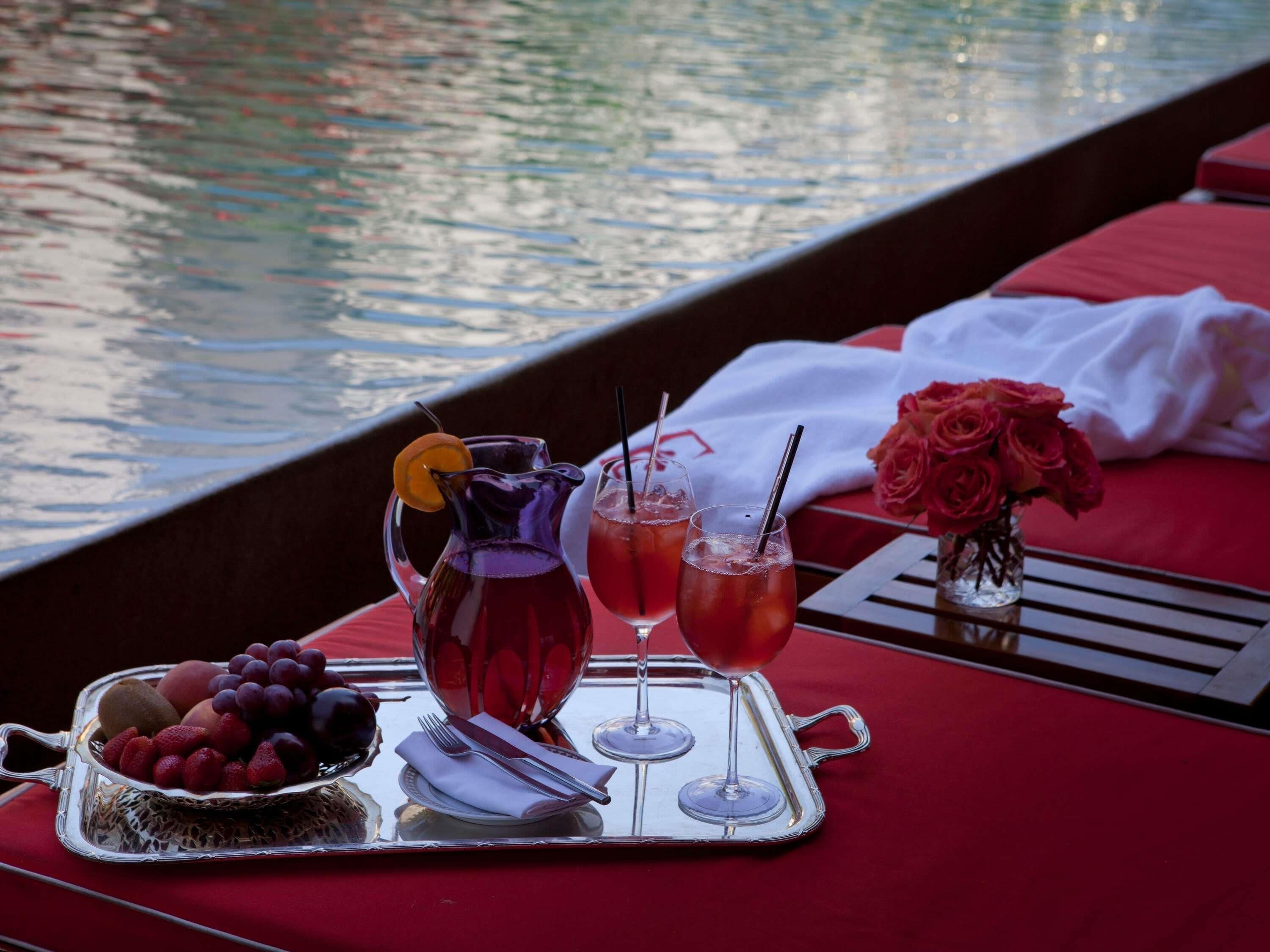 A dining setup with a tray of fruit, two drinks, and a pitcher on a boat.