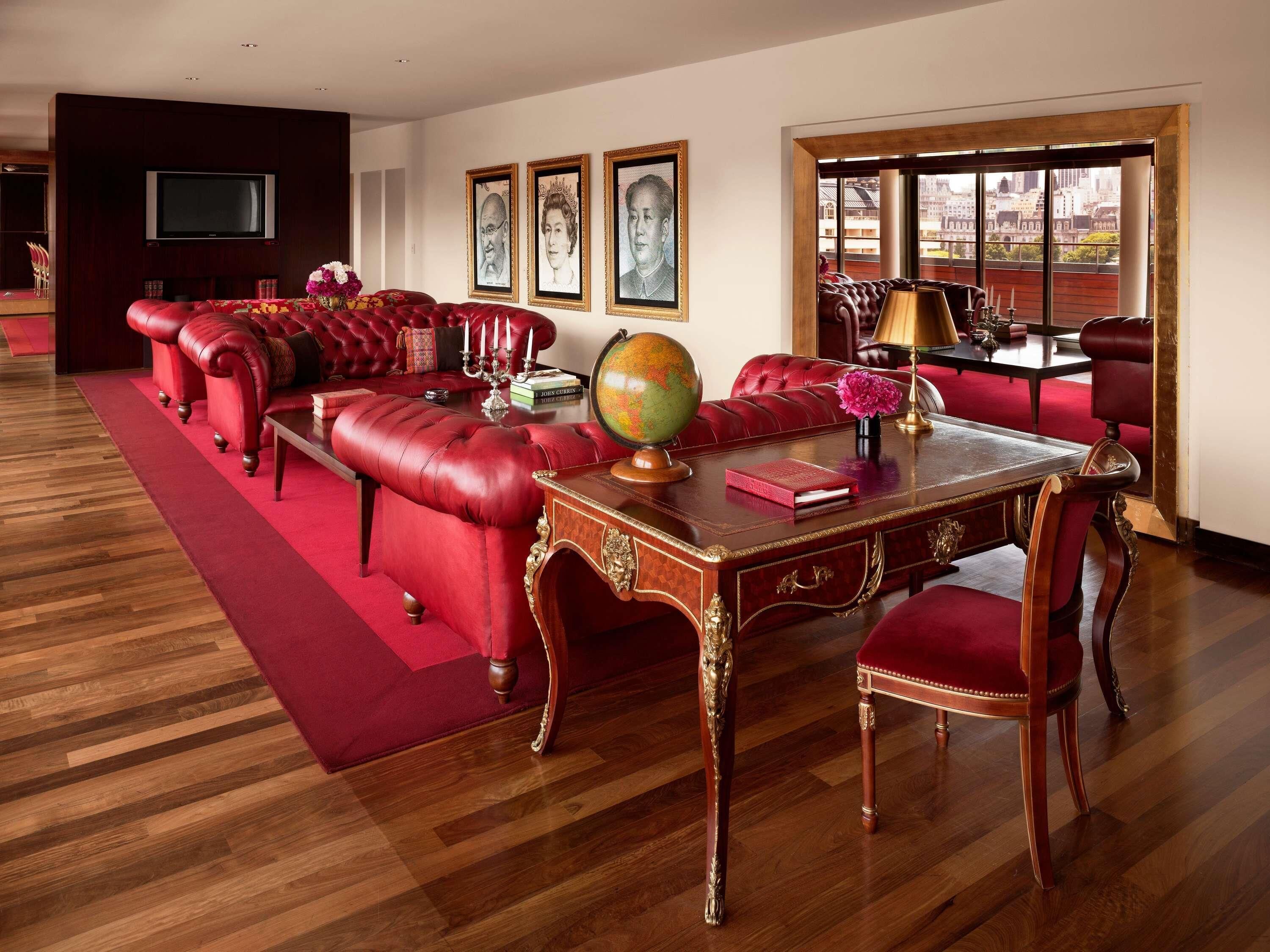 A room with a red leather sofa, a wooden desk with a globe, and framed portraits on the wall.