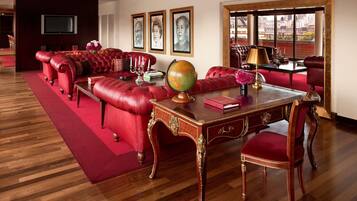 A room with a red leather sofa, a wooden desk with a globe, and framed portraits on the wall.
