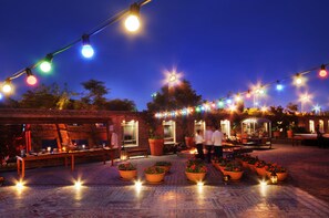 Un patio al aire libre con luces colgantes, plantas en macetas y una pared de ladrillo.
