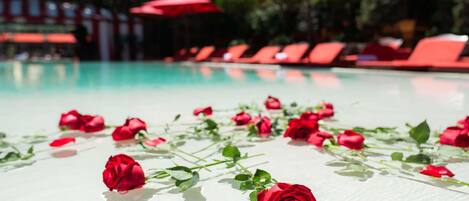 A pool area with red umbrellas and lounge chairs.