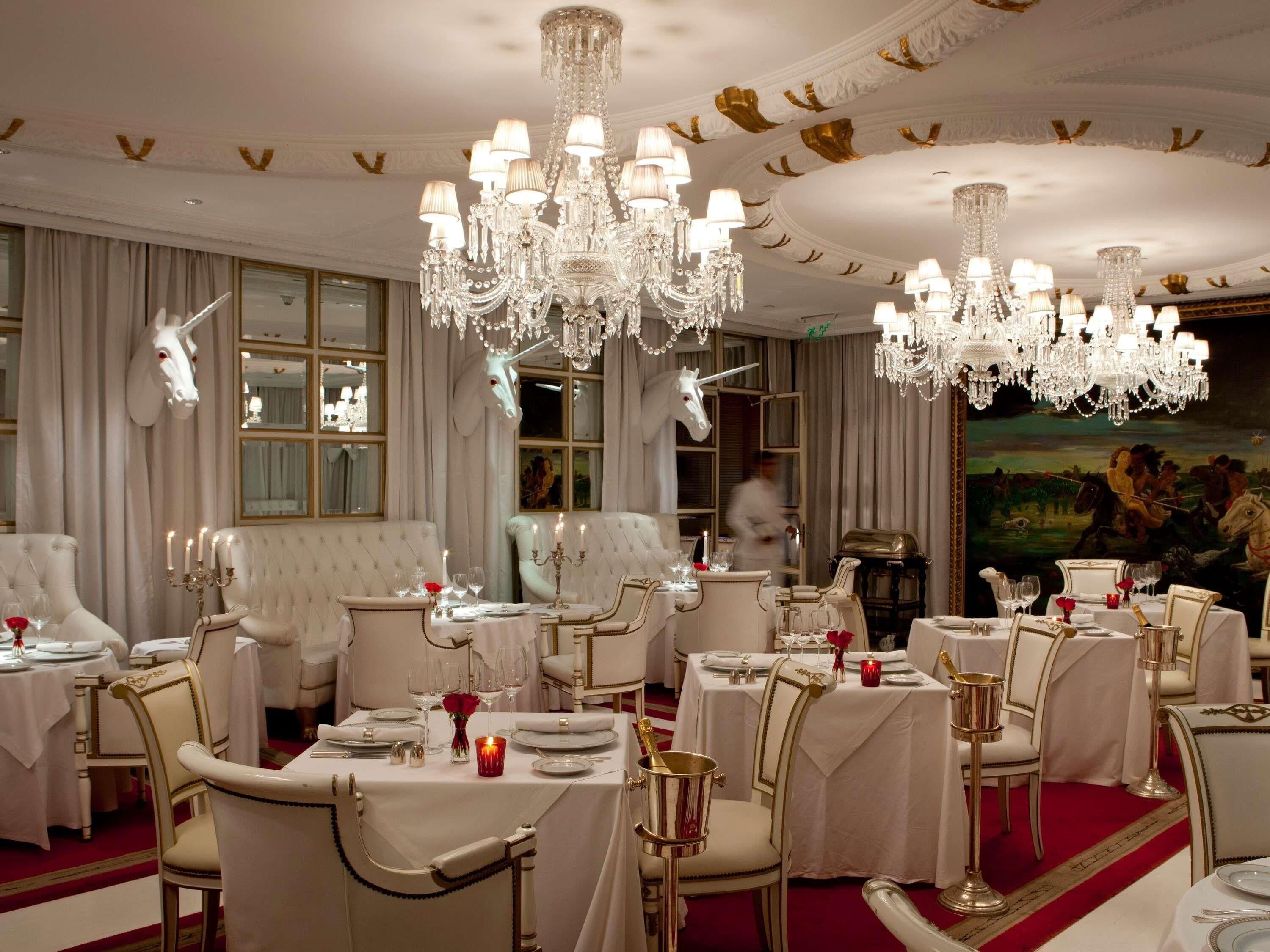 Un comedor lujoso con candelabros ornamentados, sillas blancas tapizadas y una alfombra roja.