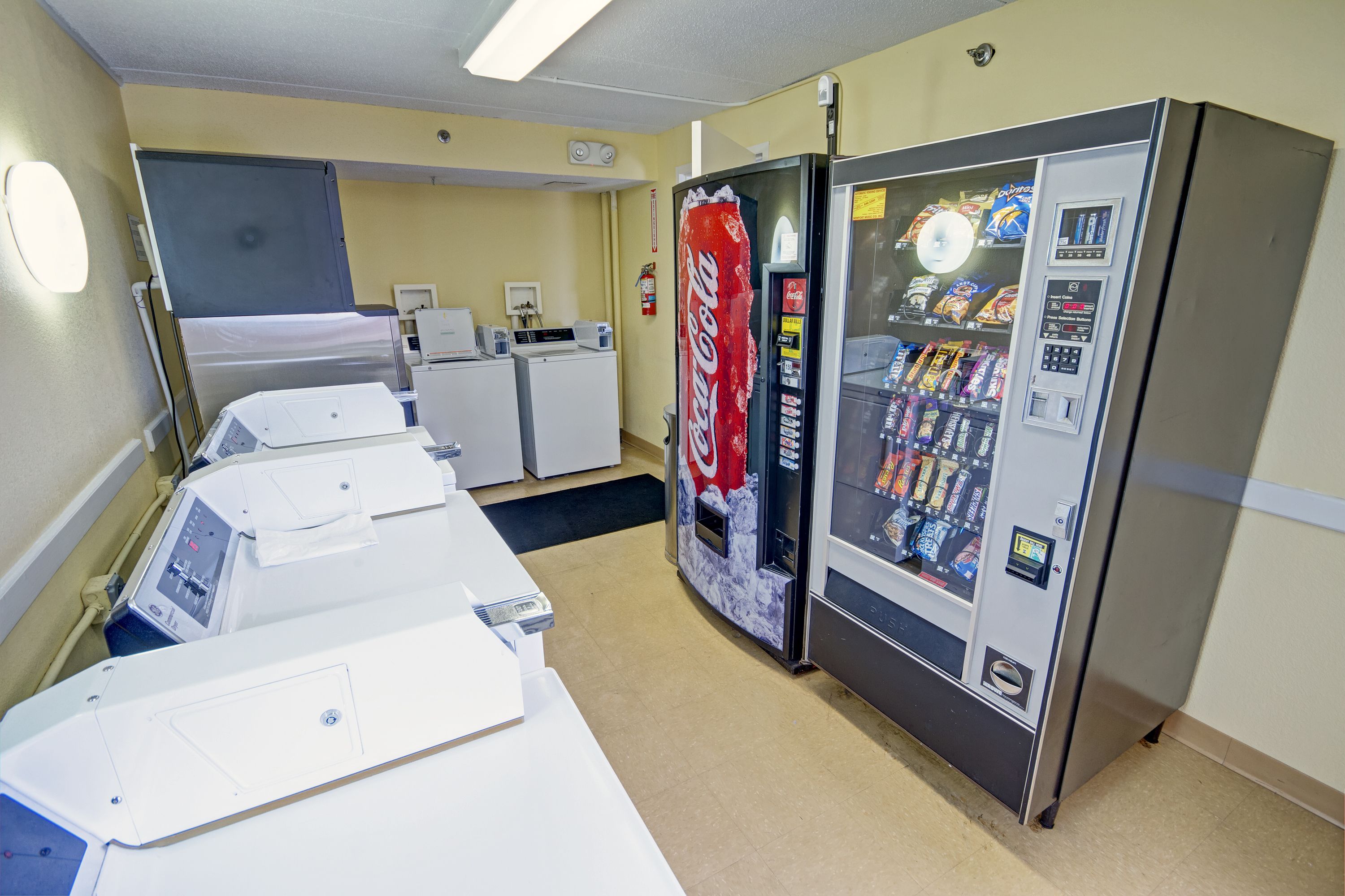 A hotel room with a bed, a washing machine, a dryer, and a vending machine.