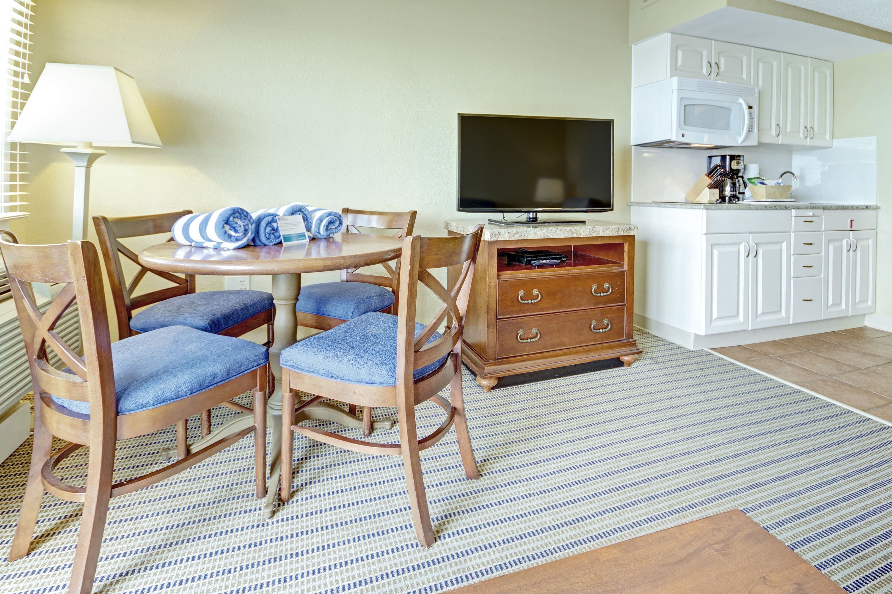 A dining area with a table, chairs, a television, and a kitchen area with cabinets and a microwave.