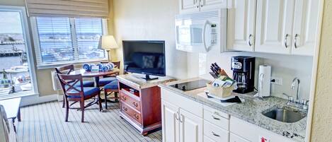 A compact kitchen with white cabinets, a microwave, a coffee maker, and a TV.