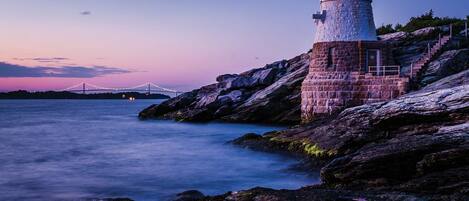 A lighthouse on rocky terrain with a bridge in the background.