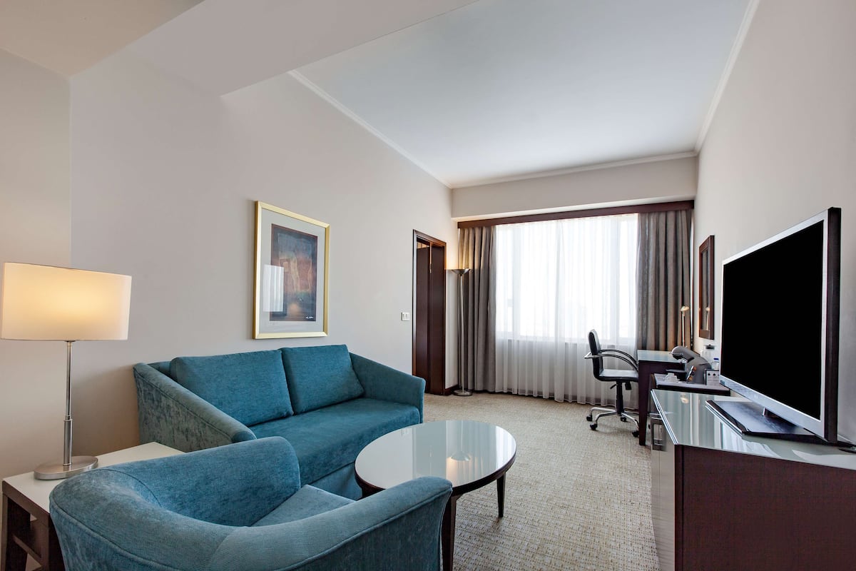 A hotel room with a sofa, a chair, a desk, a television, and a window with curtains.