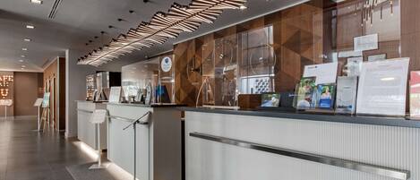 Un área de recepción moderna con un separador de vidrio, un mostrador de recepción y una pantalla digital que muestra información.