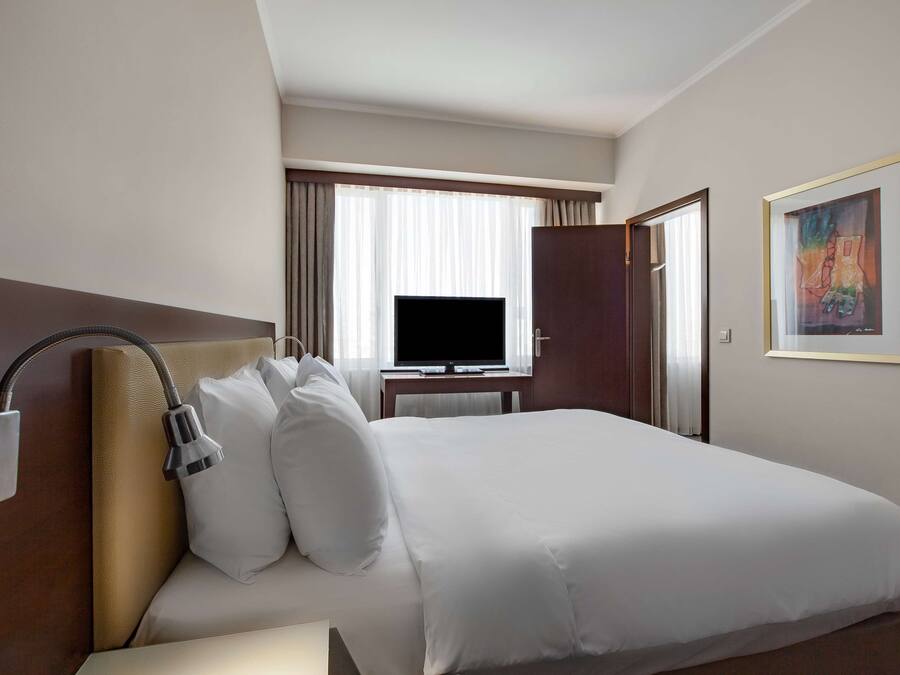 A hotel room with a large bed, a flat-screen TV, a desk, and a painting on the wall.