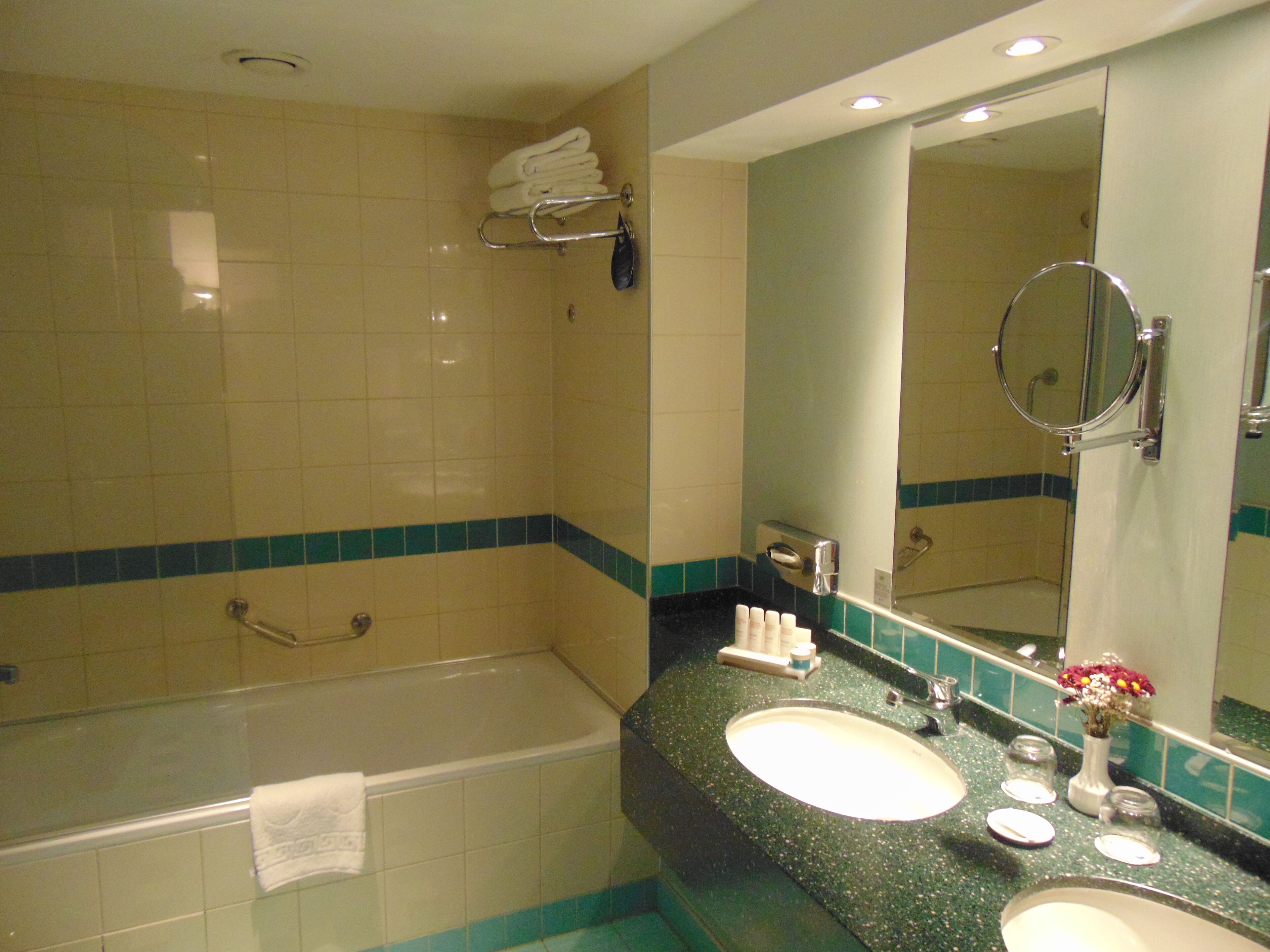 A bathroom with a bathtub, two sinks, a vanity mirror, and a towel rack.