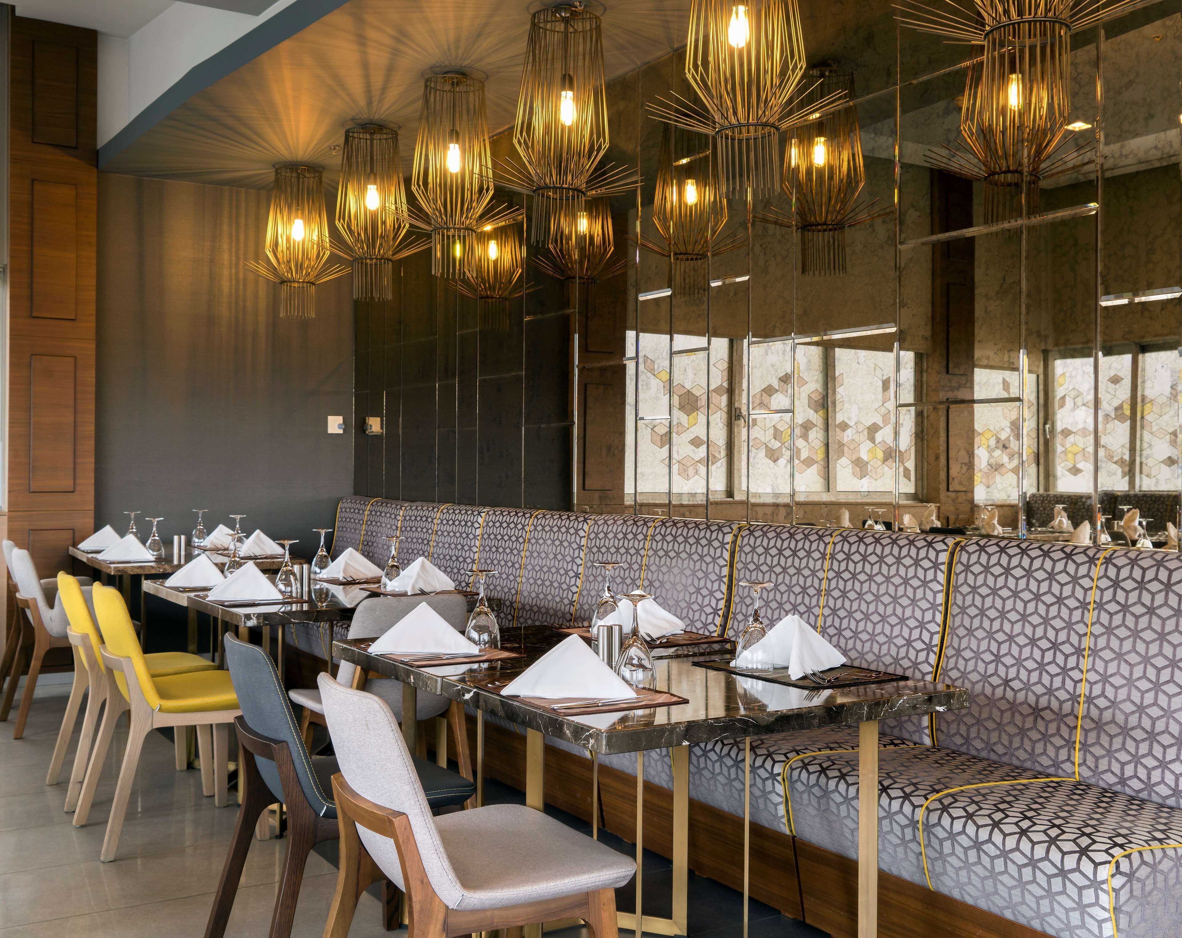 A restaurant with a long dining area, multiple tables, and a patterned bench seating area.