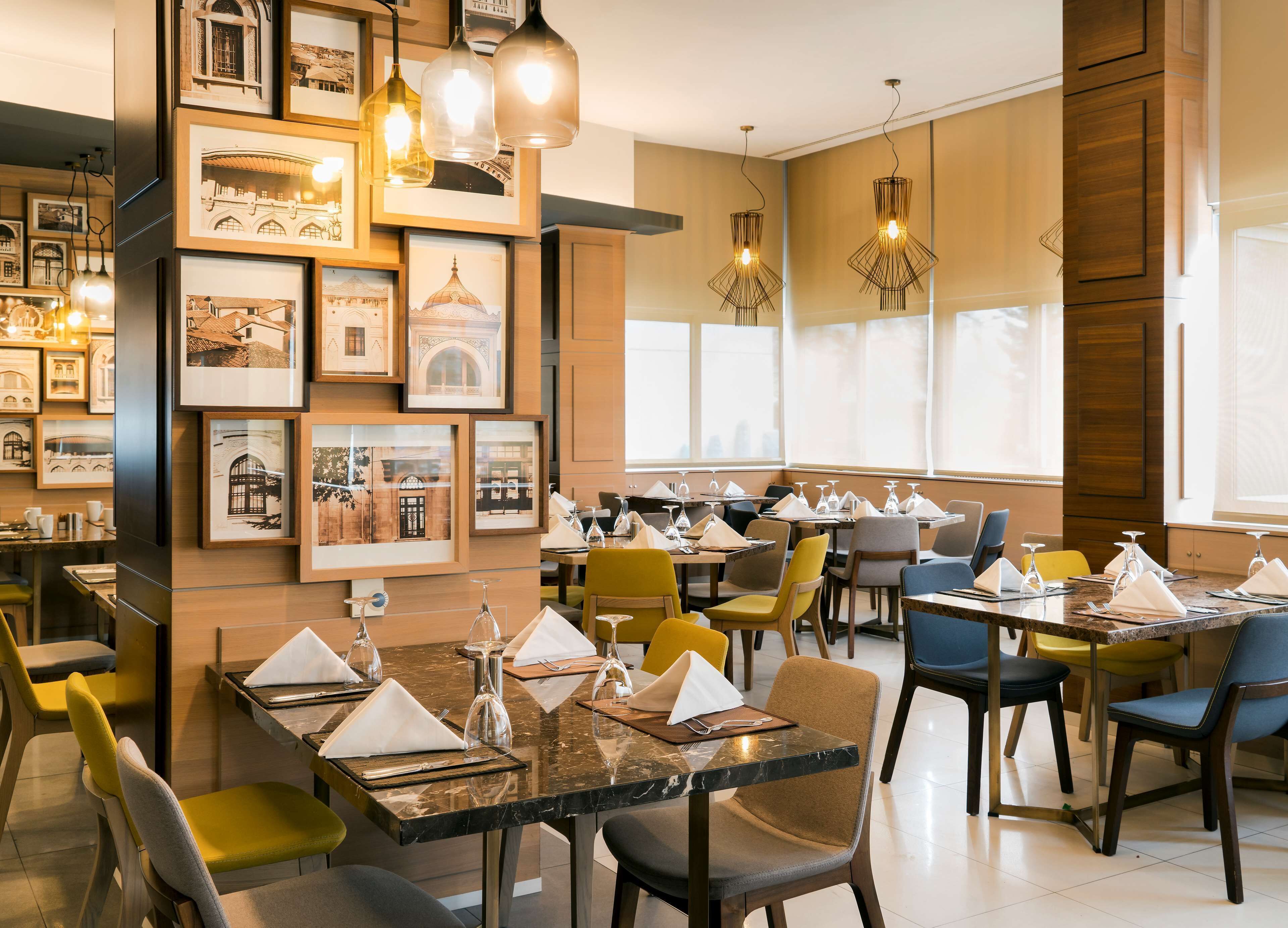 Un restaurante con varias mesas dispuestas para comer, cuadros en la pared e iluminación colgante.