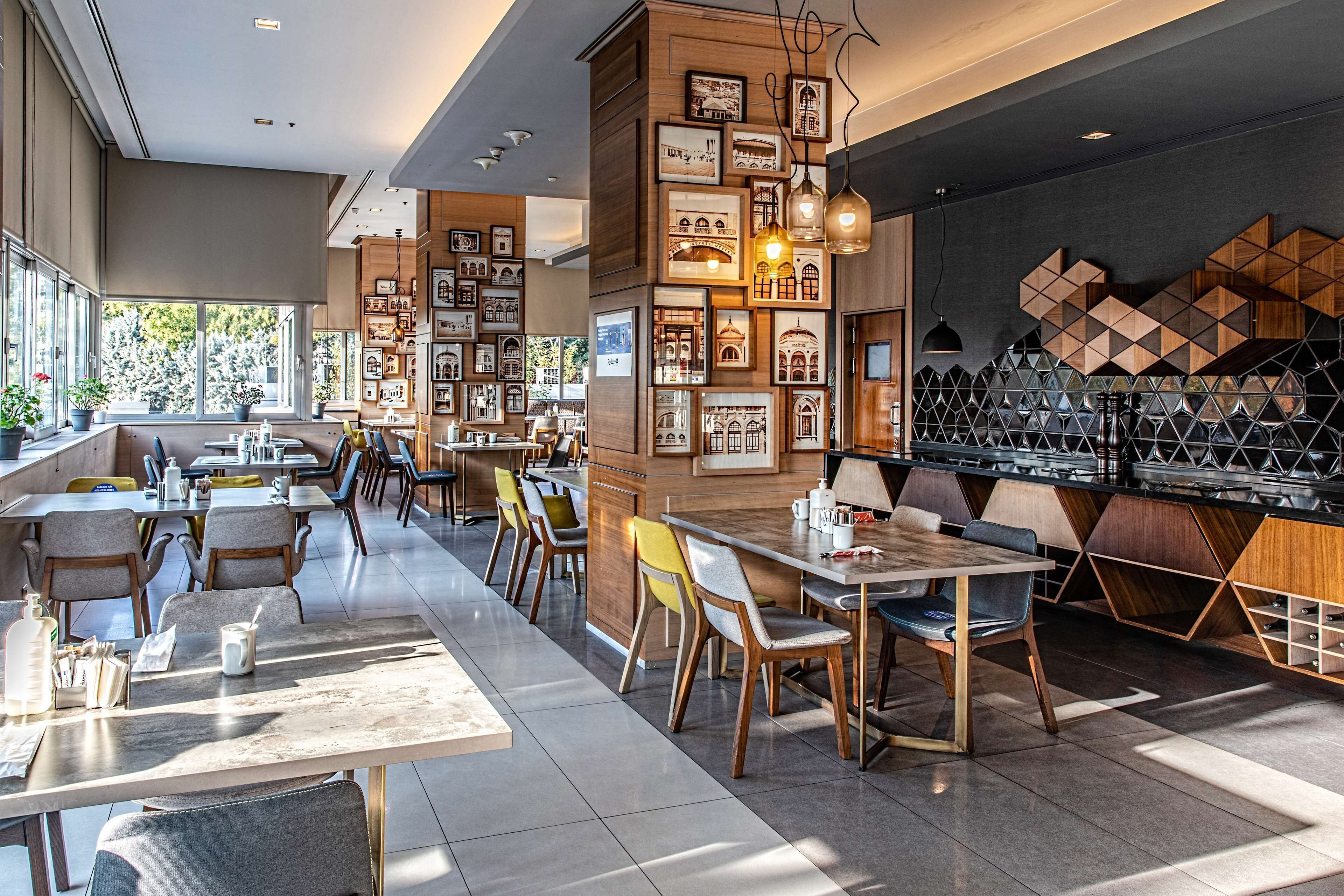 A modern restaurant with a long communal table, individual seating, and a bar area.