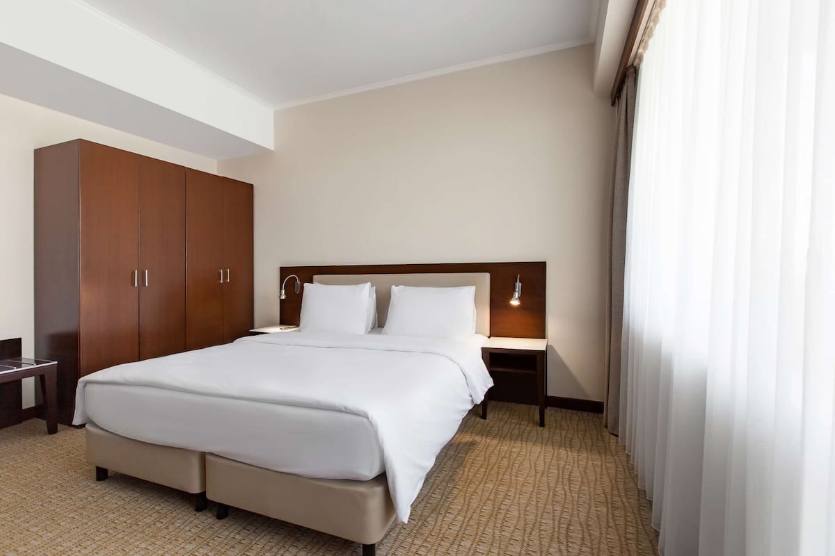 A hotel room with a large bed, a wardrobe, a bedside table, and a lamp.