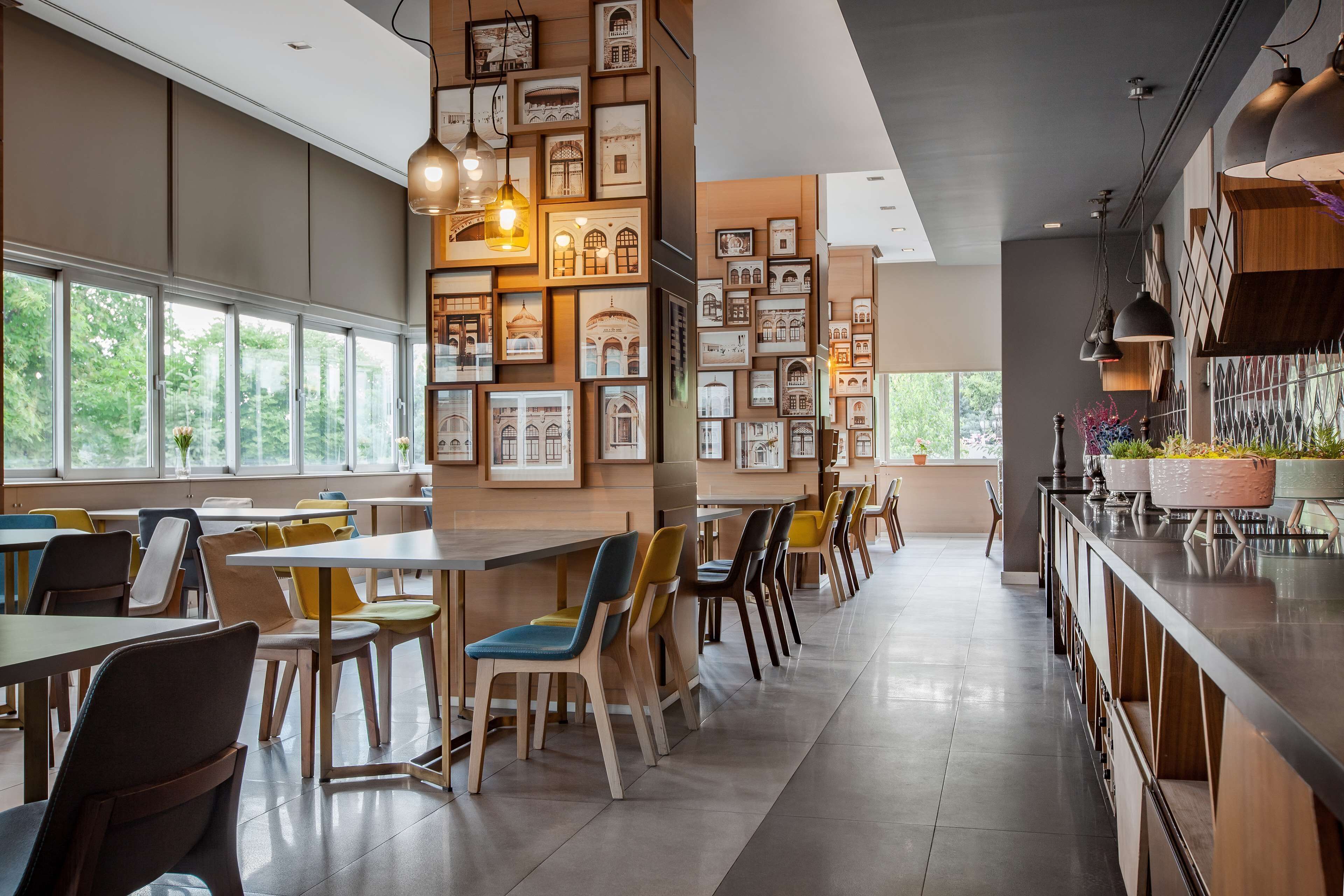 Un comedor moderno con mesas y sillas, cuadros en las paredes y amplios ventanales.