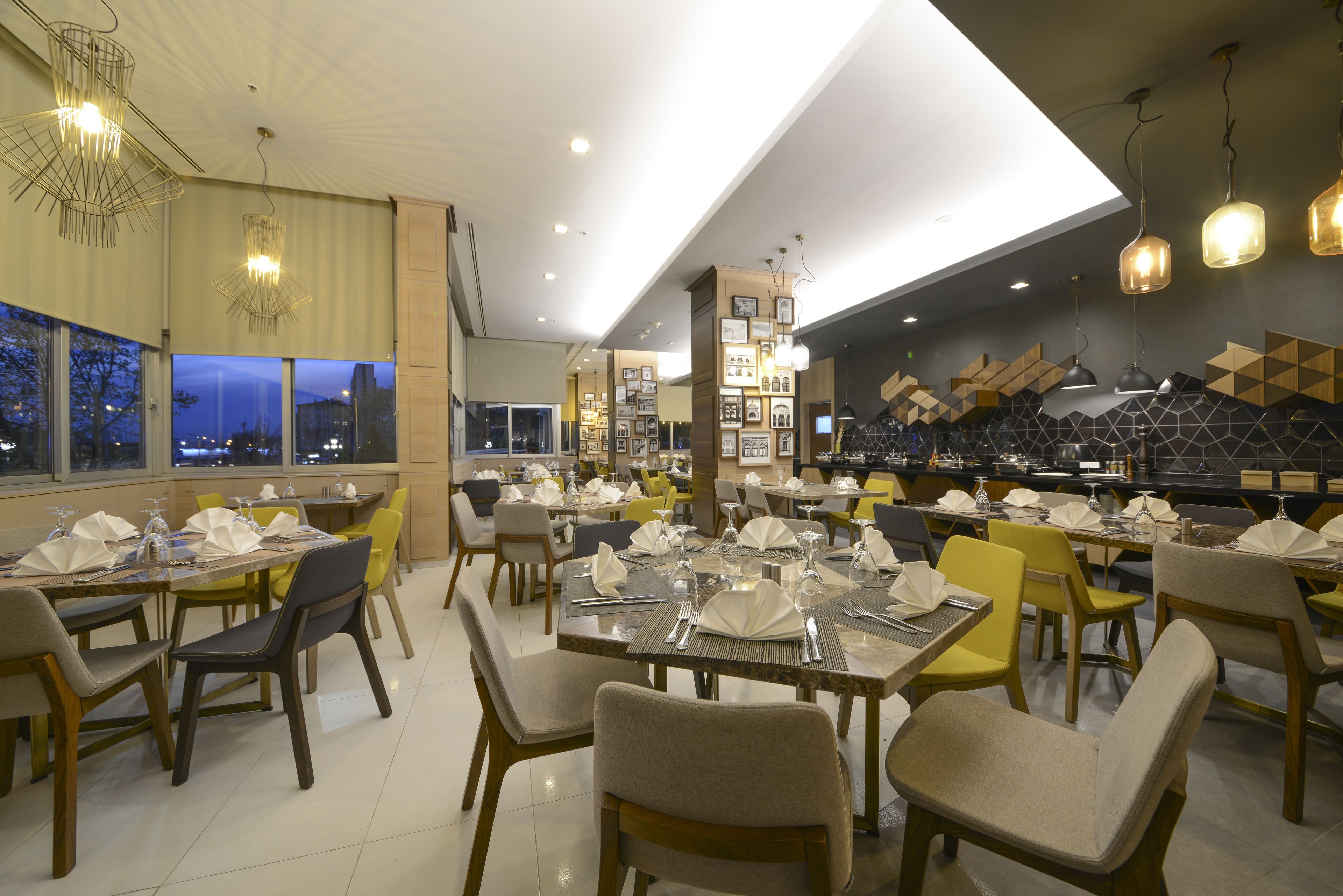 A restaurant with multiple dining tables set for guests, featuring a modern interior design with geometric wall patterns and pendant lighting.