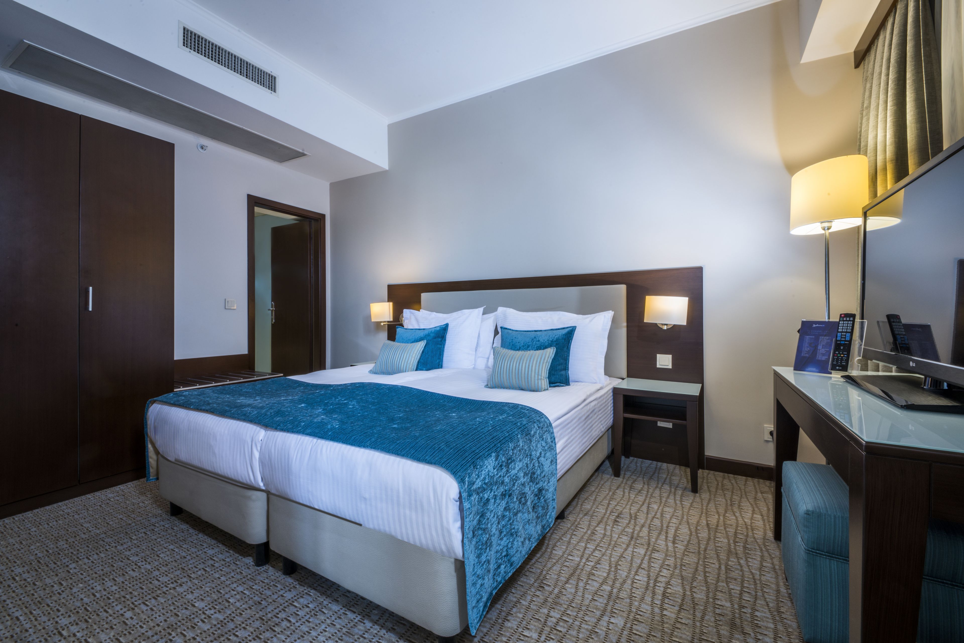 Een hotelkamer met een groot bed, een bureau, een stoel, een lamp en een kledingkast.