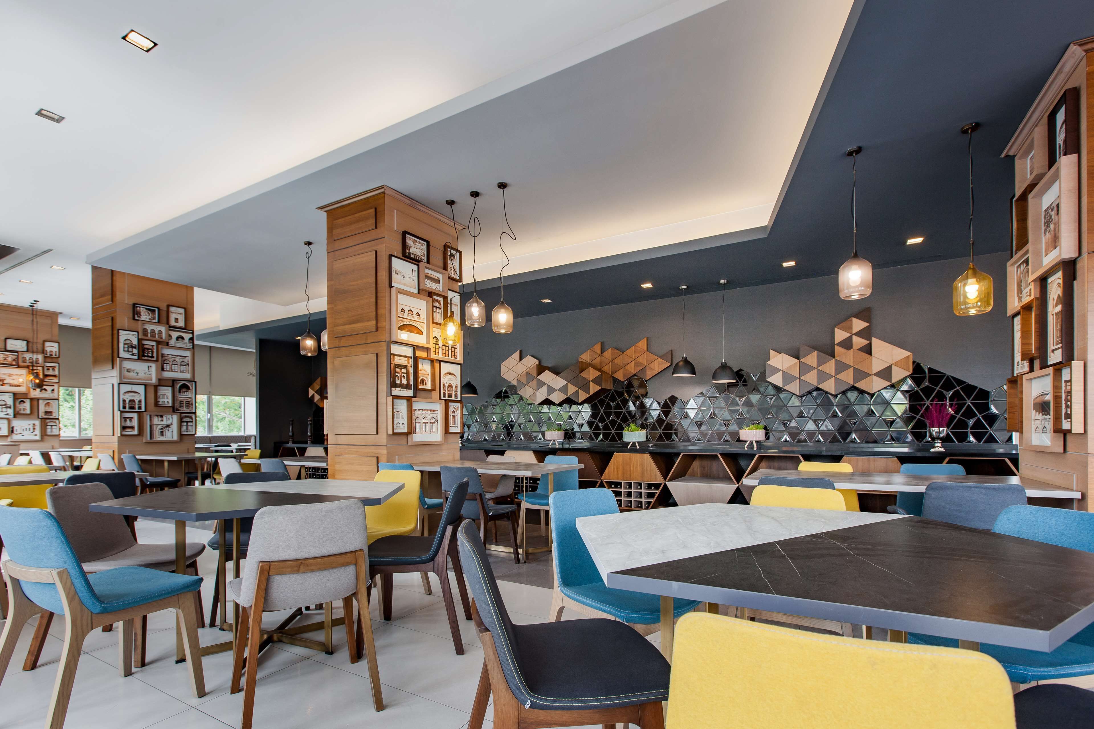 Een modern restaurant met meerdere eettafels en stoelen, een bar en een muur versierd met geometrische patronen en ingekaderde foto's.