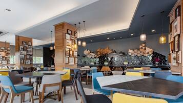 Een modern restaurant met meerdere eettafels en stoelen, een bar en een muur versierd met geometrische patronen en ingekaderde foto's.