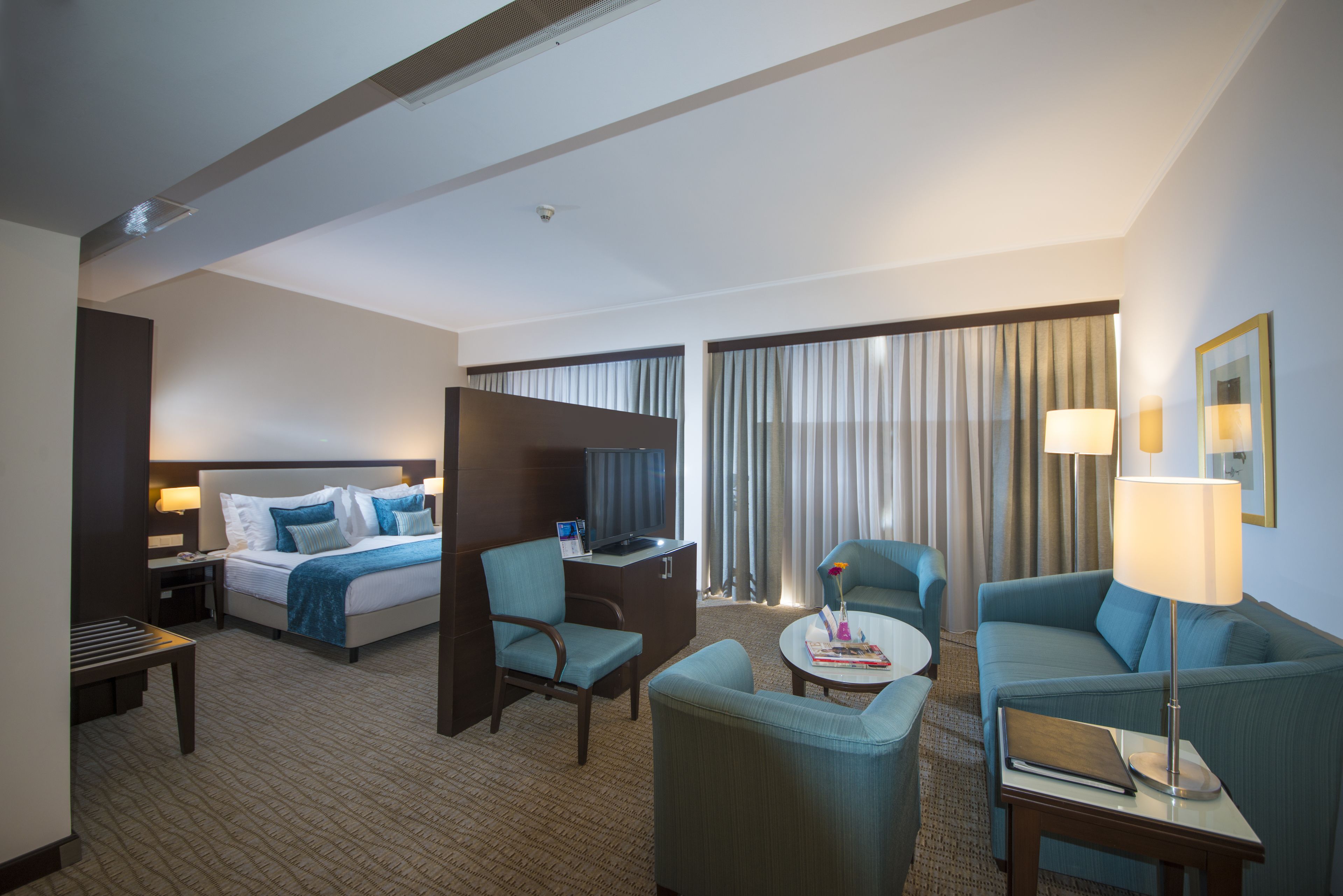 Habitación de hotel con cama, dos sillones, escritorio, televisor y ventana con cortinas.