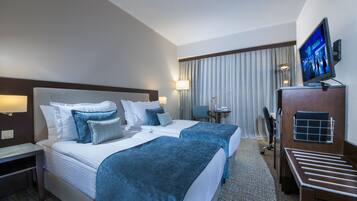 Habitación de hotel con dos camas, un escritorio, una silla, un televisor y una ventana con cortinas.