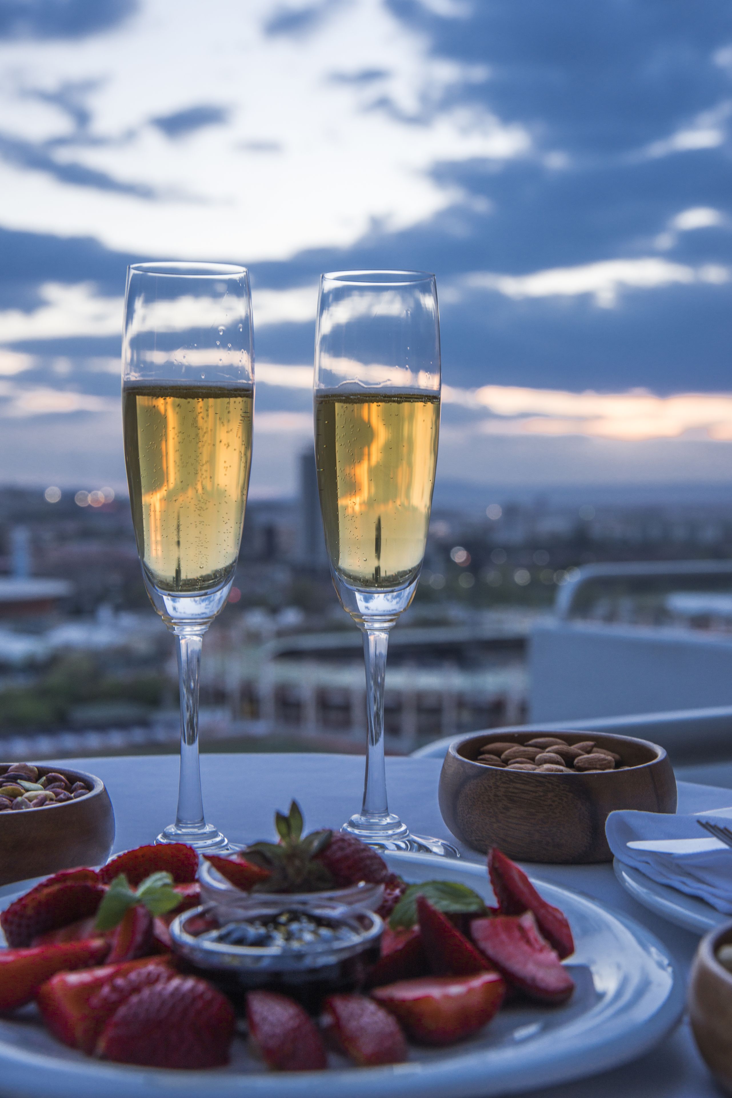 Two champagne flutes on a table with a city view in the background.