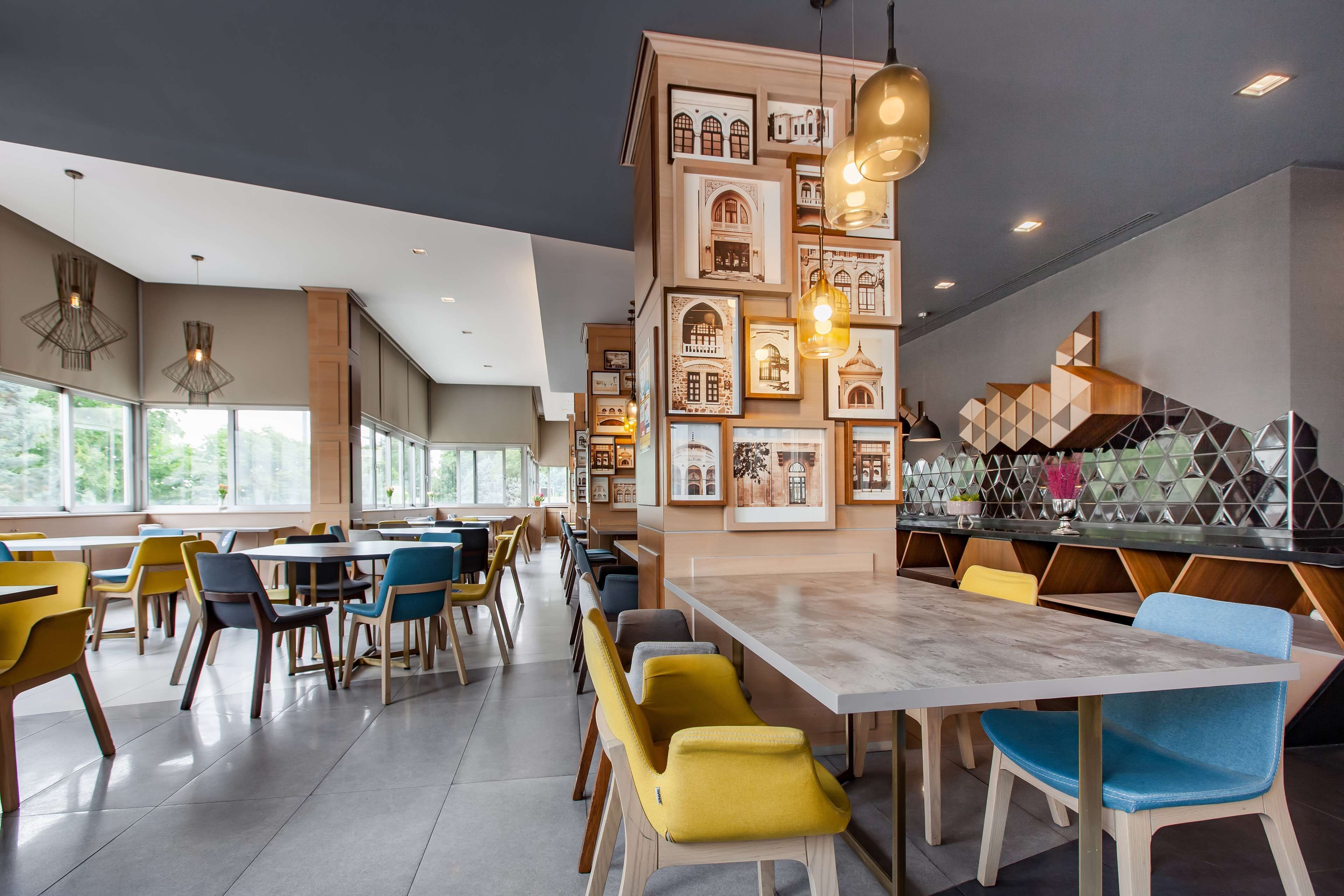 Una moderna sala da pranzo con diversi tavoli e sedie, quadri appesi alle pareti e lampade a sospensione.