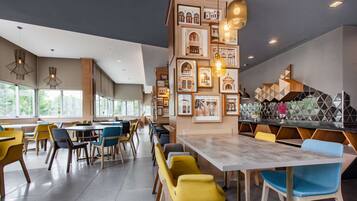 Una moderna sala da pranzo con diversi tavoli e sedie, quadri appesi alle pareti e lampade a sospensione.