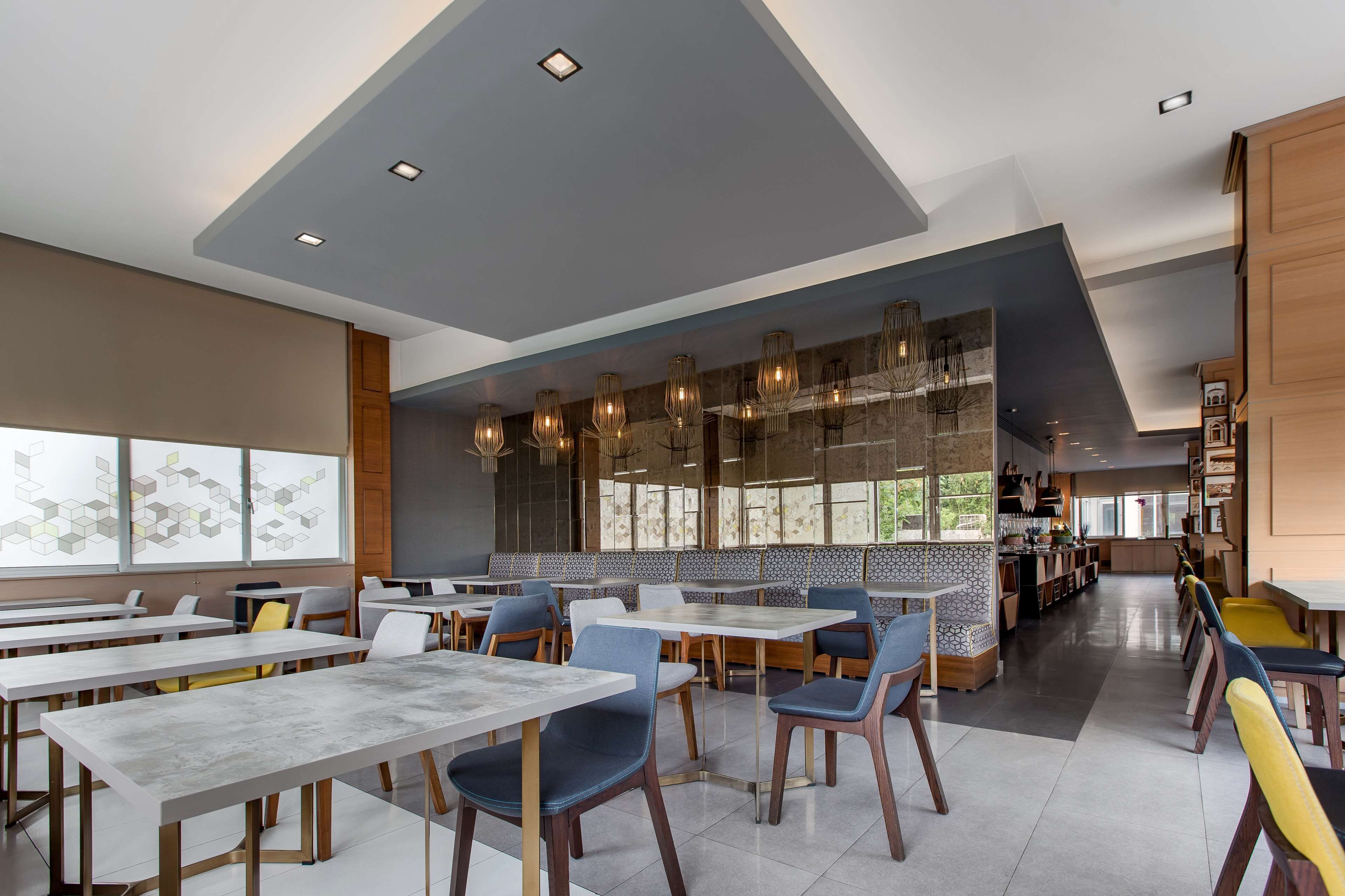 A modern restaurant with high tables and chairs, a central seating area with a patterned wall, and a kitchen visible in the background.