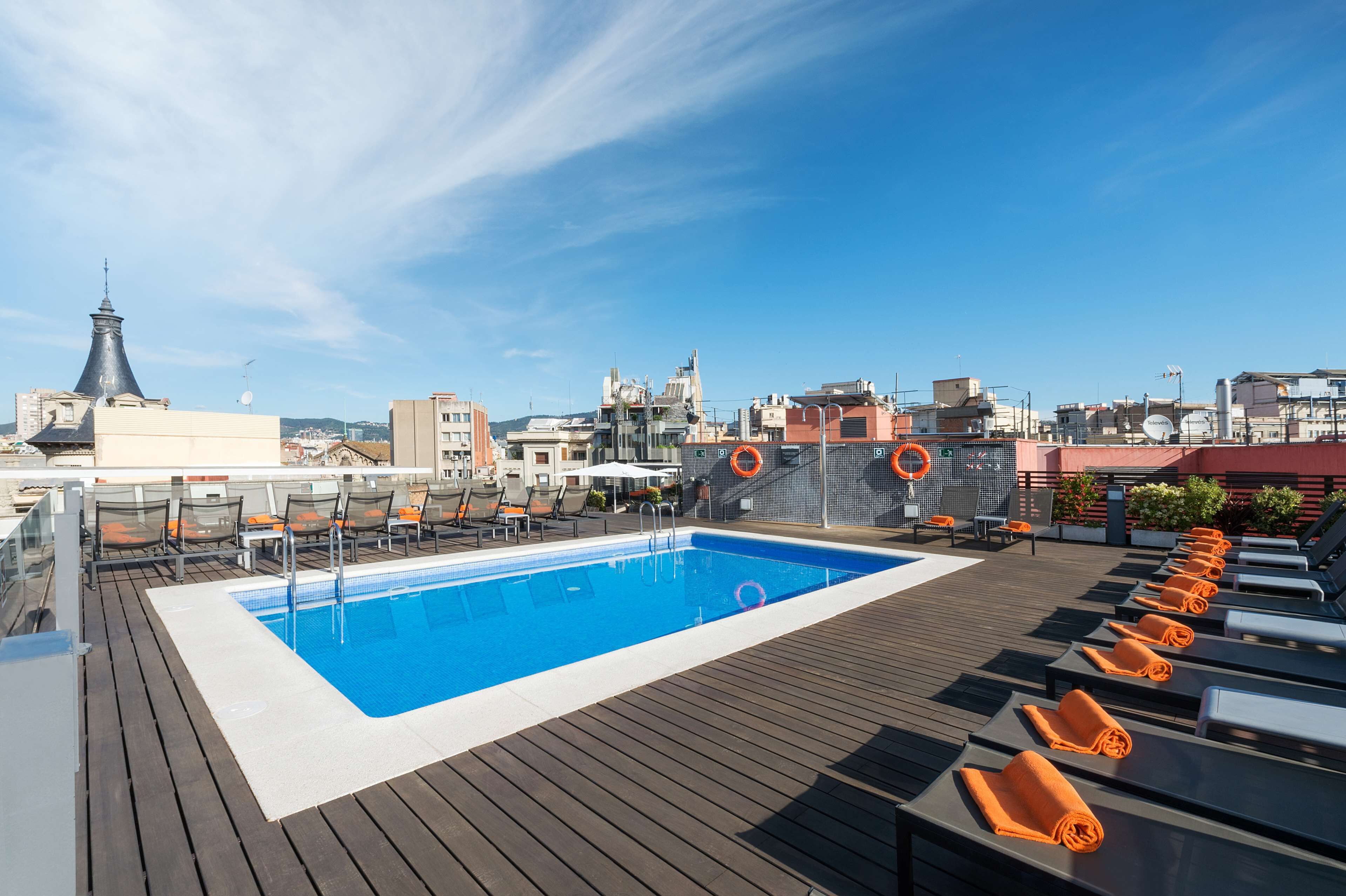 A rooftop pool with lounge chairs and a city view.
