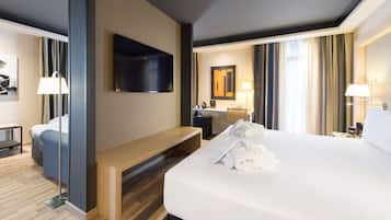 Ett modernt hotellrum med en stor säng, ett skrivbord, en platt-TV, en bänk och ett badrum som syns genom en öppen dörr.