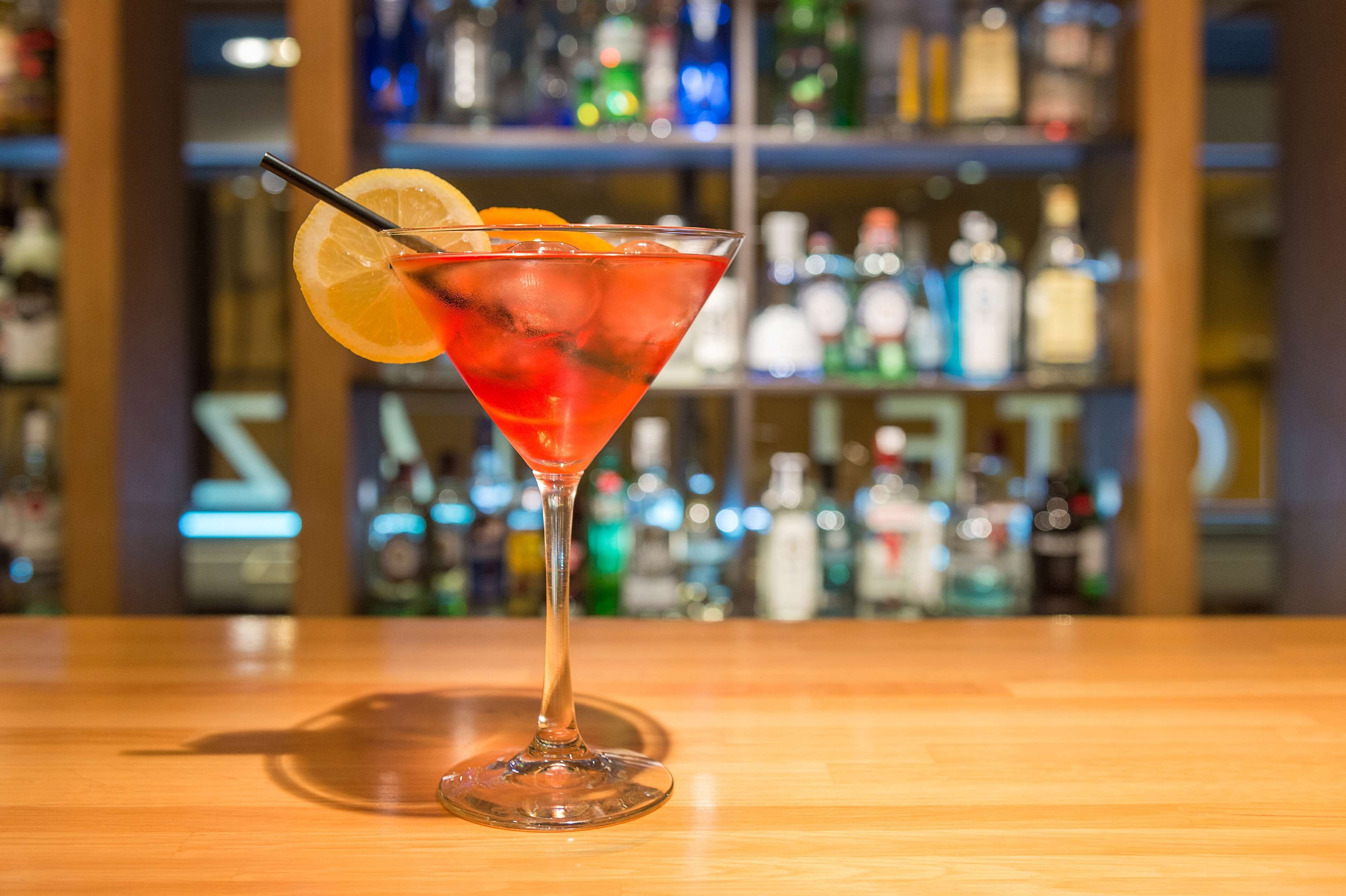 Un cóctel en una copa de martini con una rodaja de limón sobre la barra.