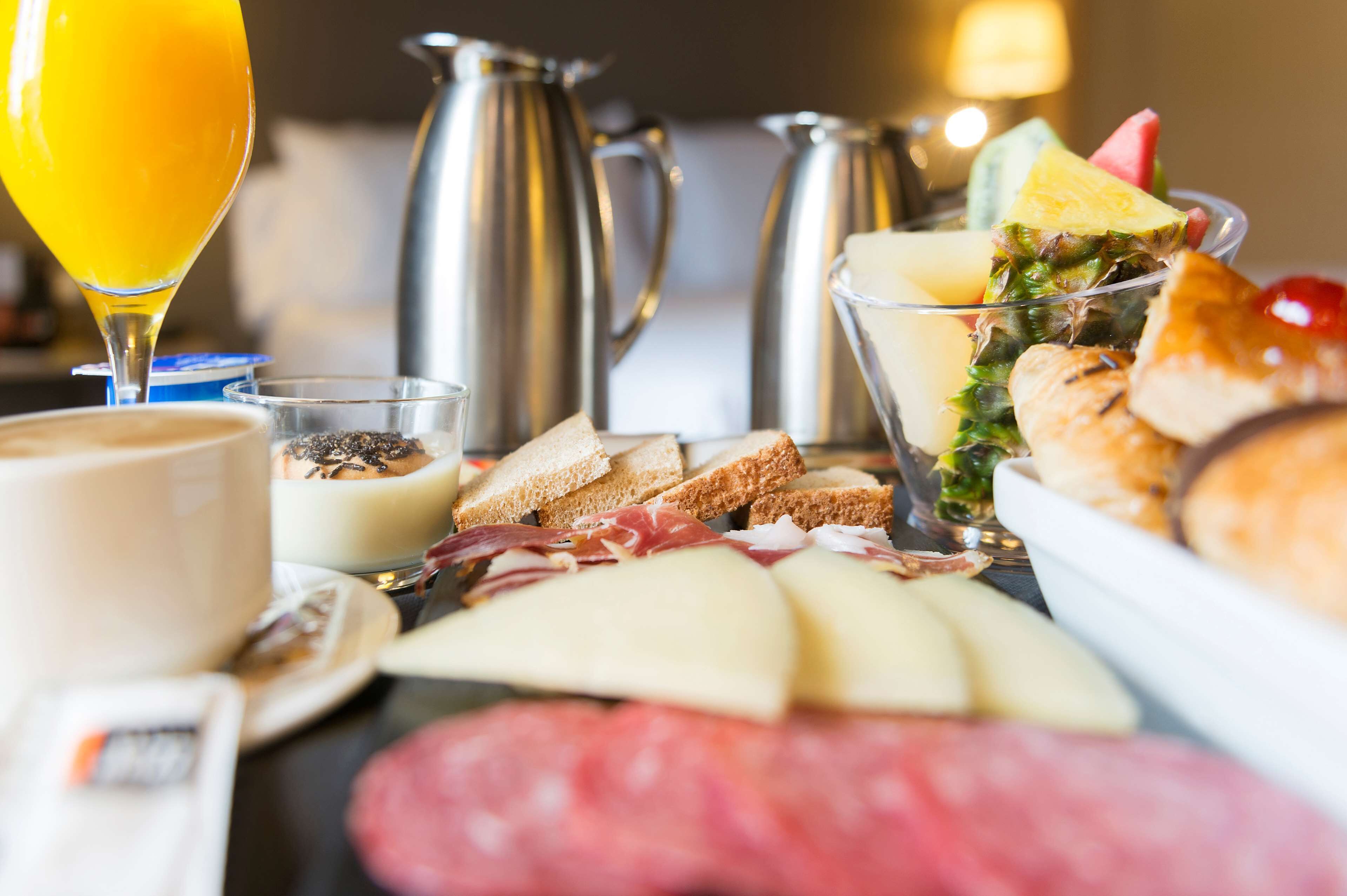 Ein Frühstücksbuffet mit verschiedenen Käsesorten, Fleisch, Brot und einem Glas Orangensaft.