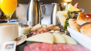 Ein Frühstücksbuffet mit verschiedenen Käsesorten, Fleisch, Brot und einem Glas Orangensaft.