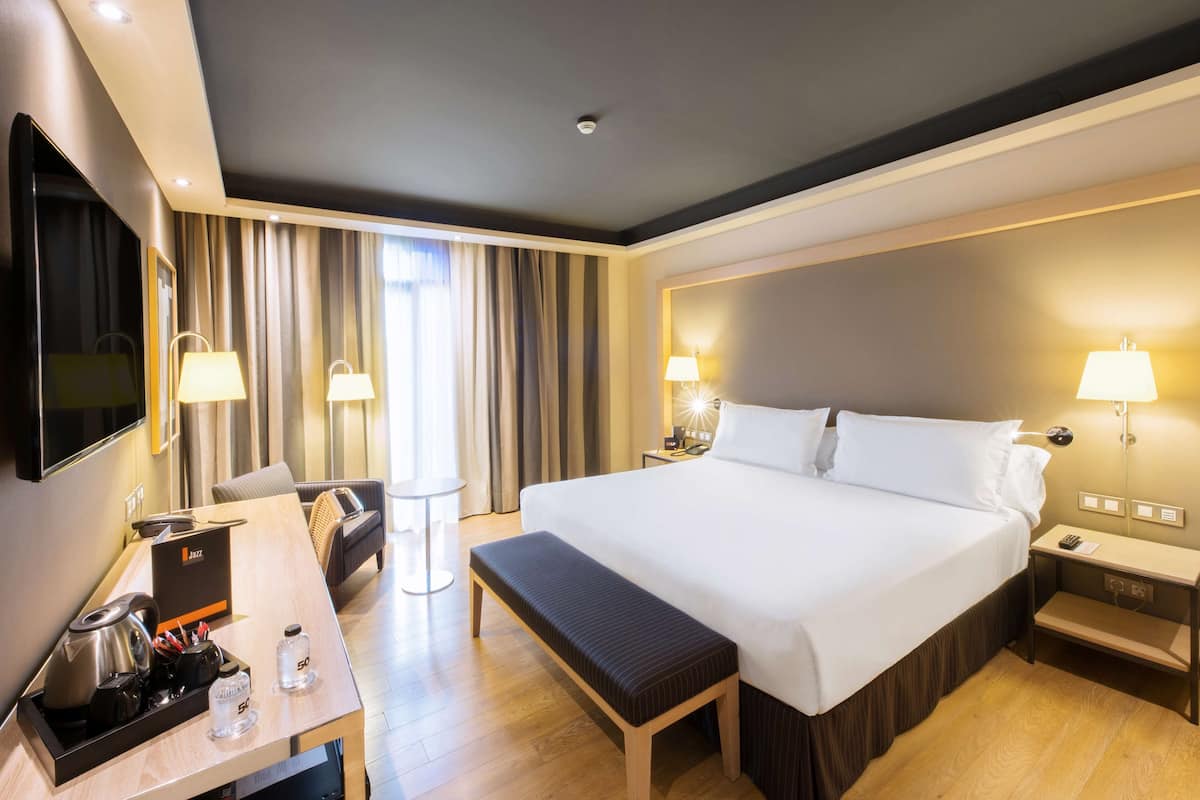 Habitación de hotel con una cama grande, lámparas de noche, un escritorio con cafetera y un televisor.