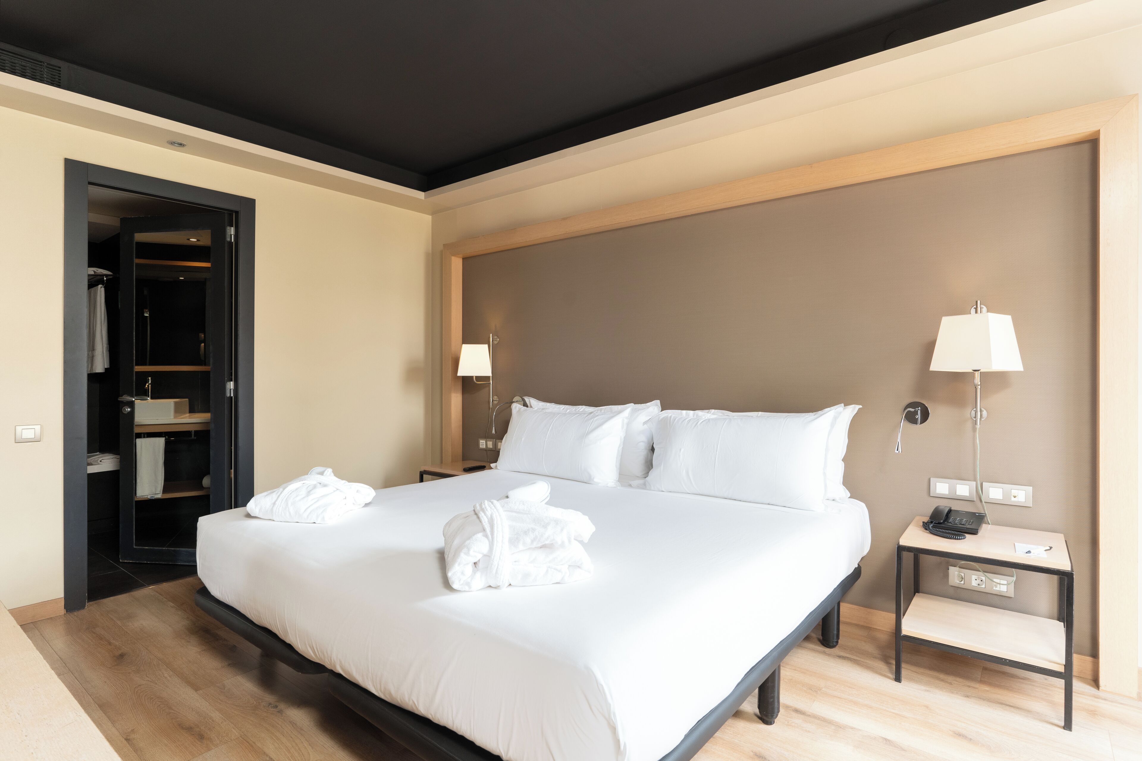 A modern hotel room with a large bed, bedside lamps, a nightstand, and a walk-in closet.