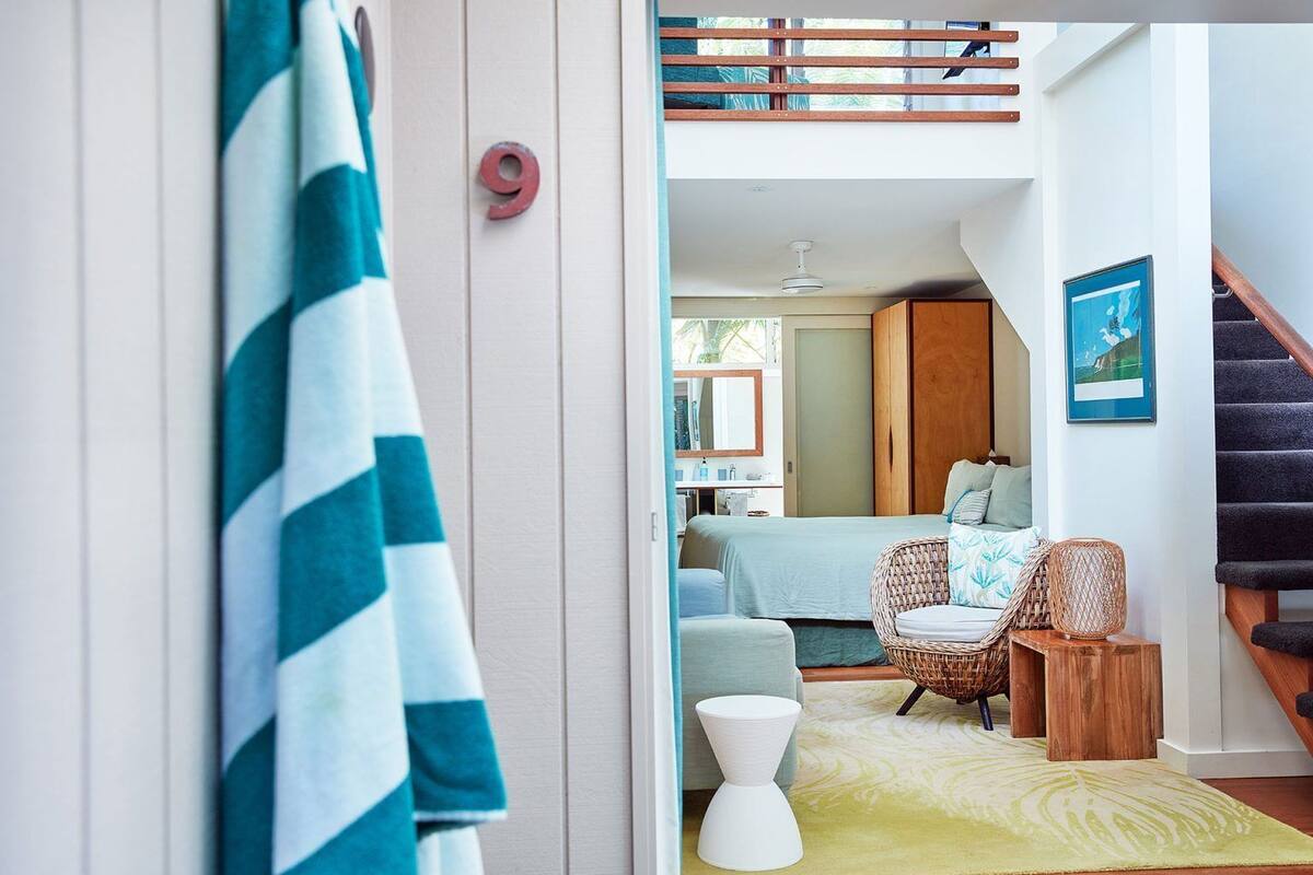 Un interior moderno con una cama, una silla de mimbre, una mesita y una escalera.